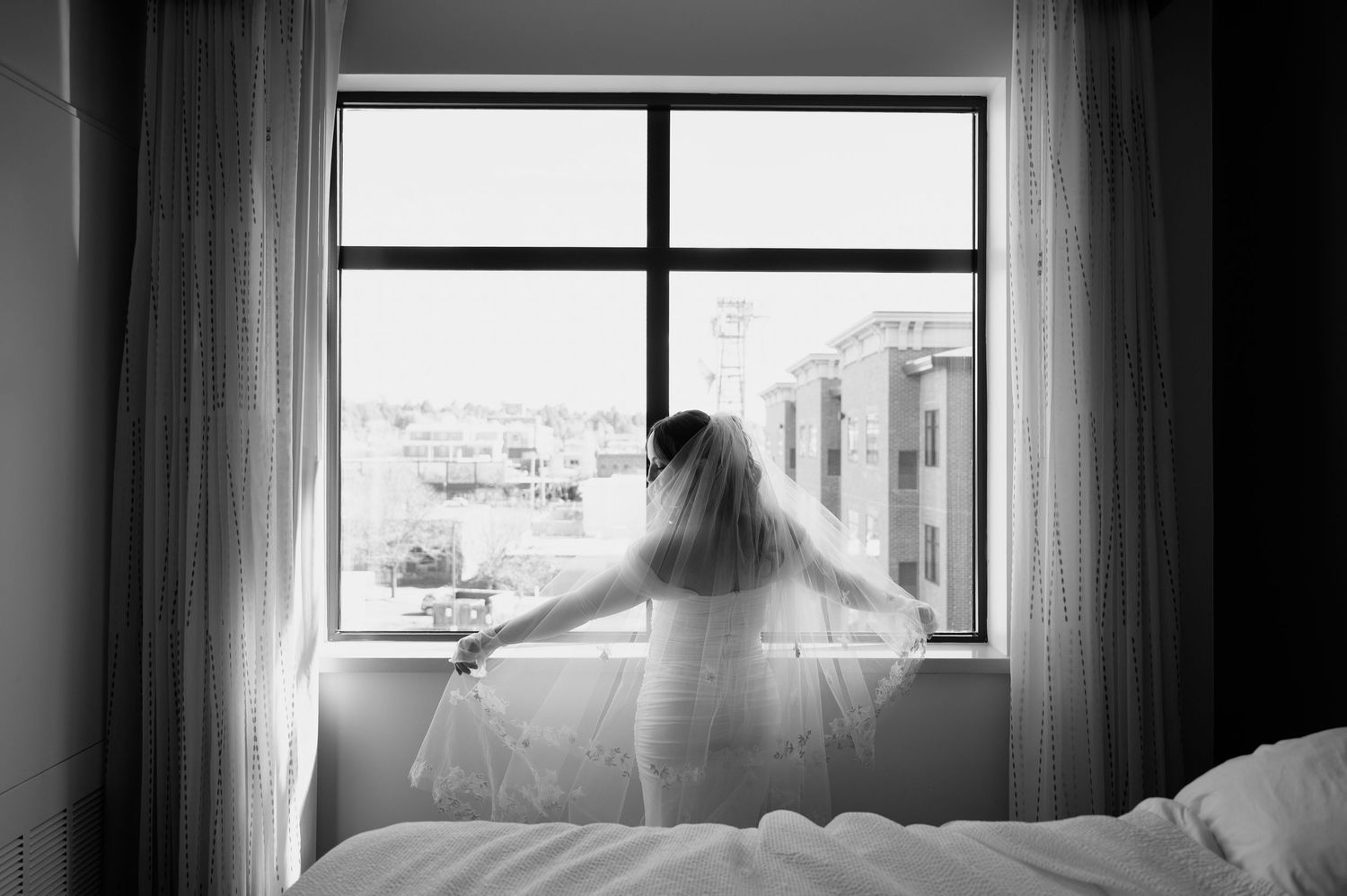 A bride in a wedding veil stands before a large window in a black and white photo in Flagstaff Arizona.