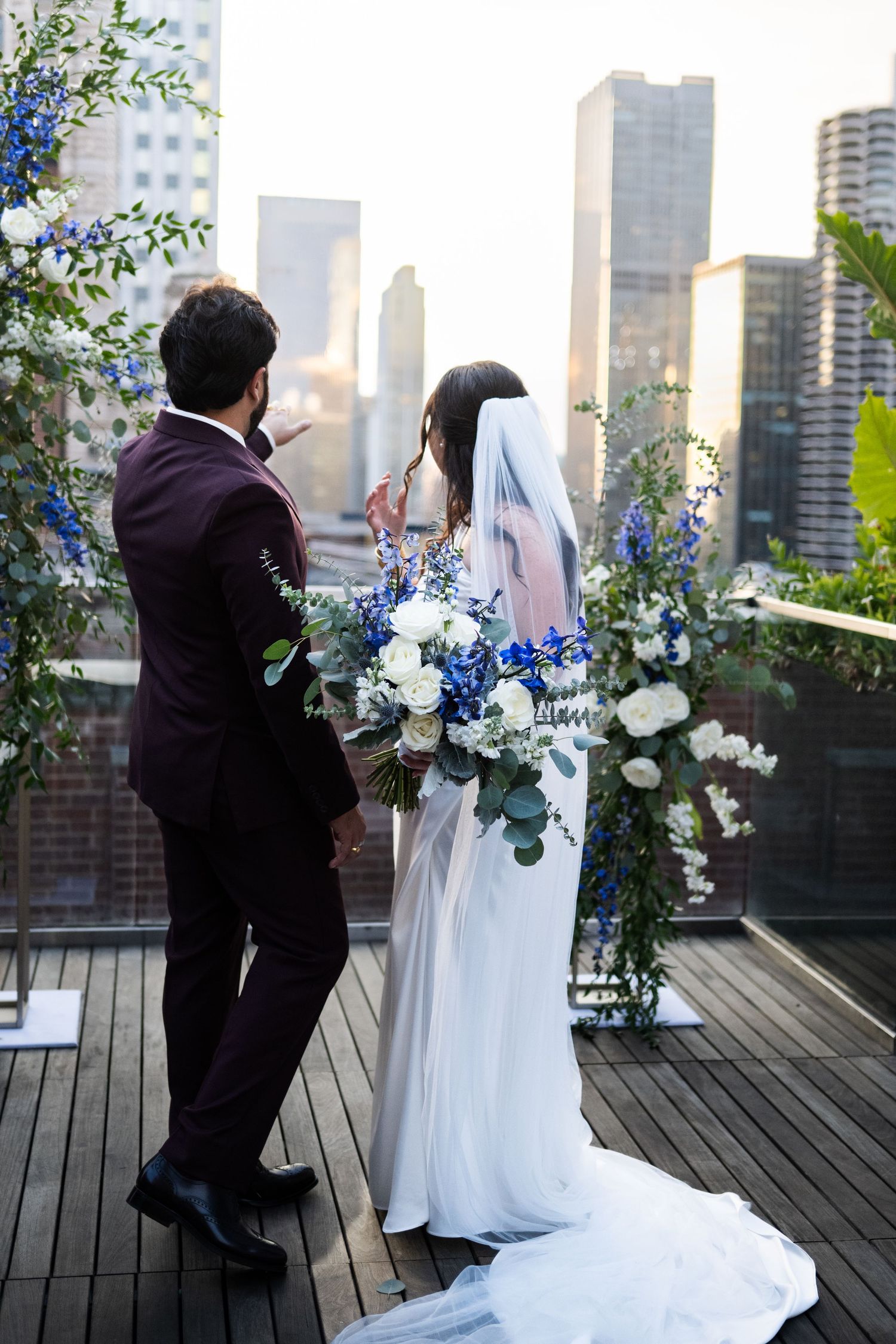 Bride and groom stand before blue and white floral arch on rooftop with city skyline view at The Pendry Hotel in Chicago Illinois.