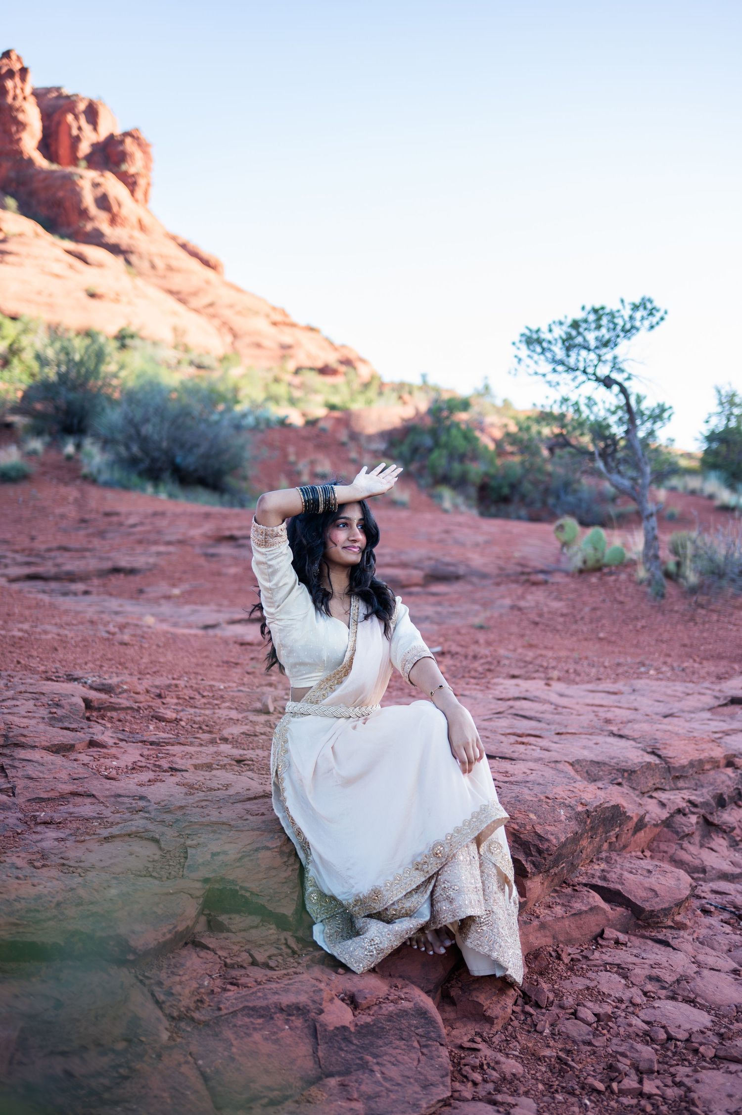 Woman in white traditional Indian attire sitting on red rocks in Sedona Arizona desert landscape.