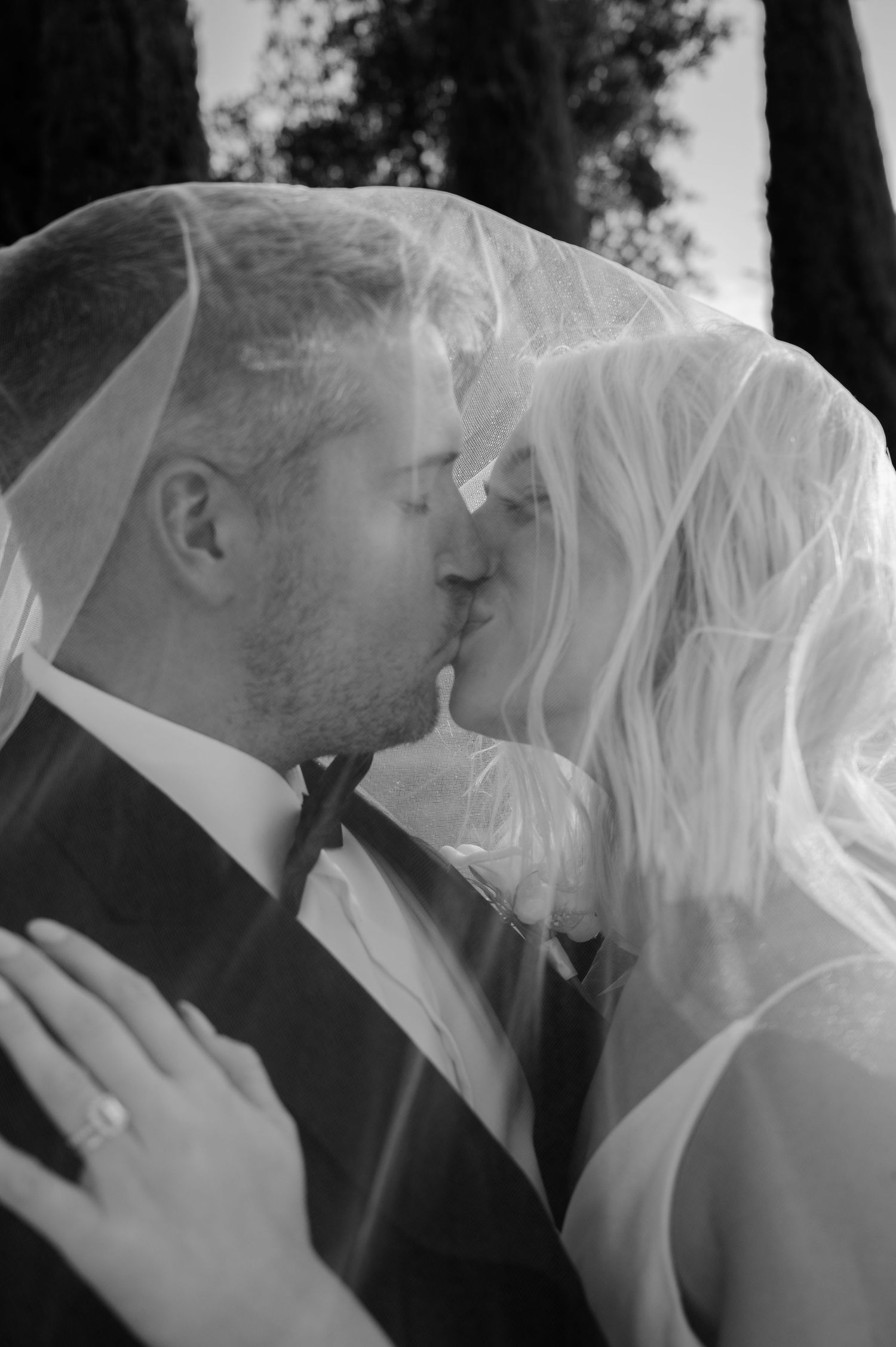 Black and white wedding photo of bride and groom kissing under a veil.