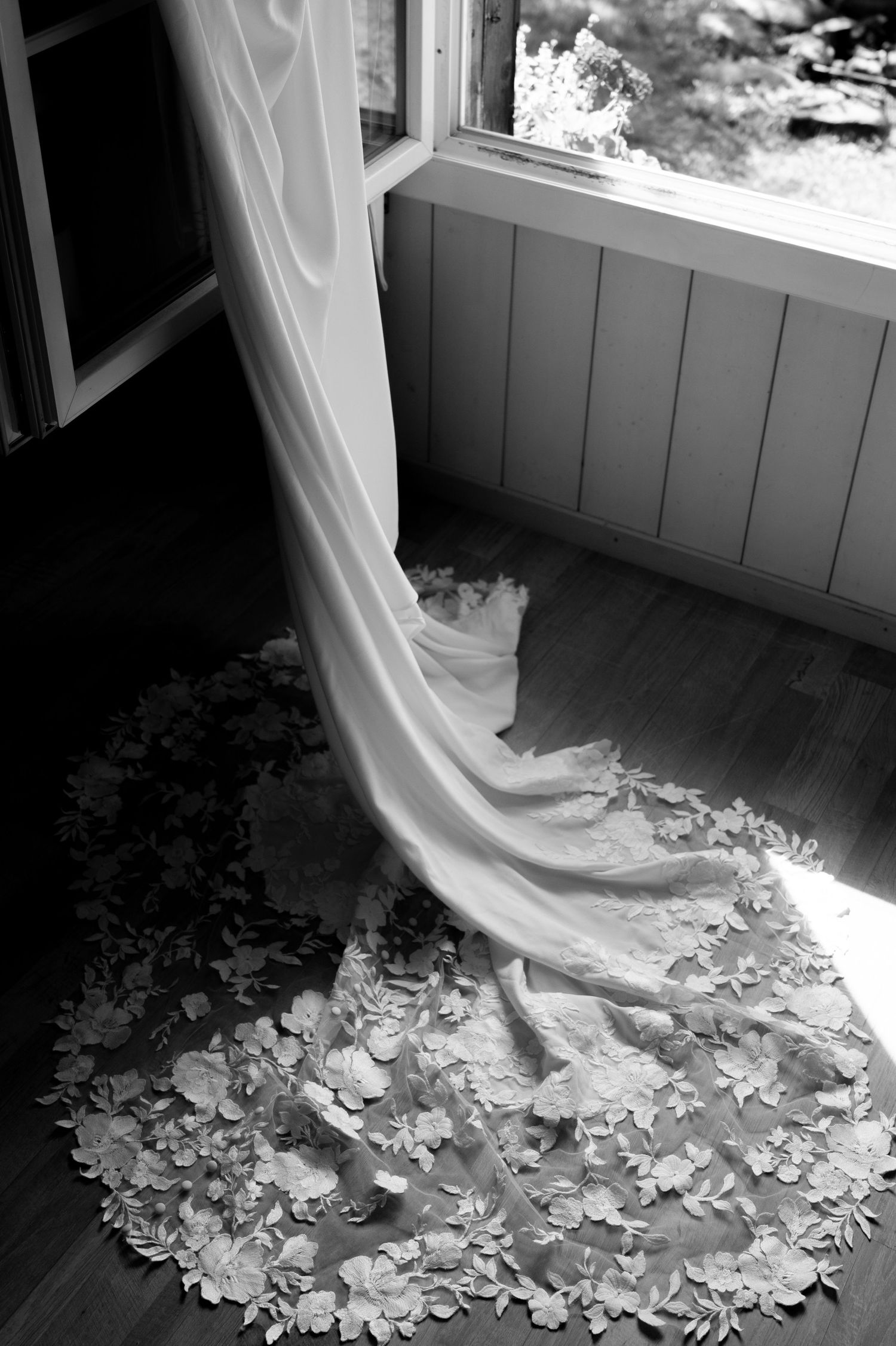Elegant floral lace cathedral wedding dress train pooling on wooden floor beside sunlit open window in Lauterbrunnen Switzerland.