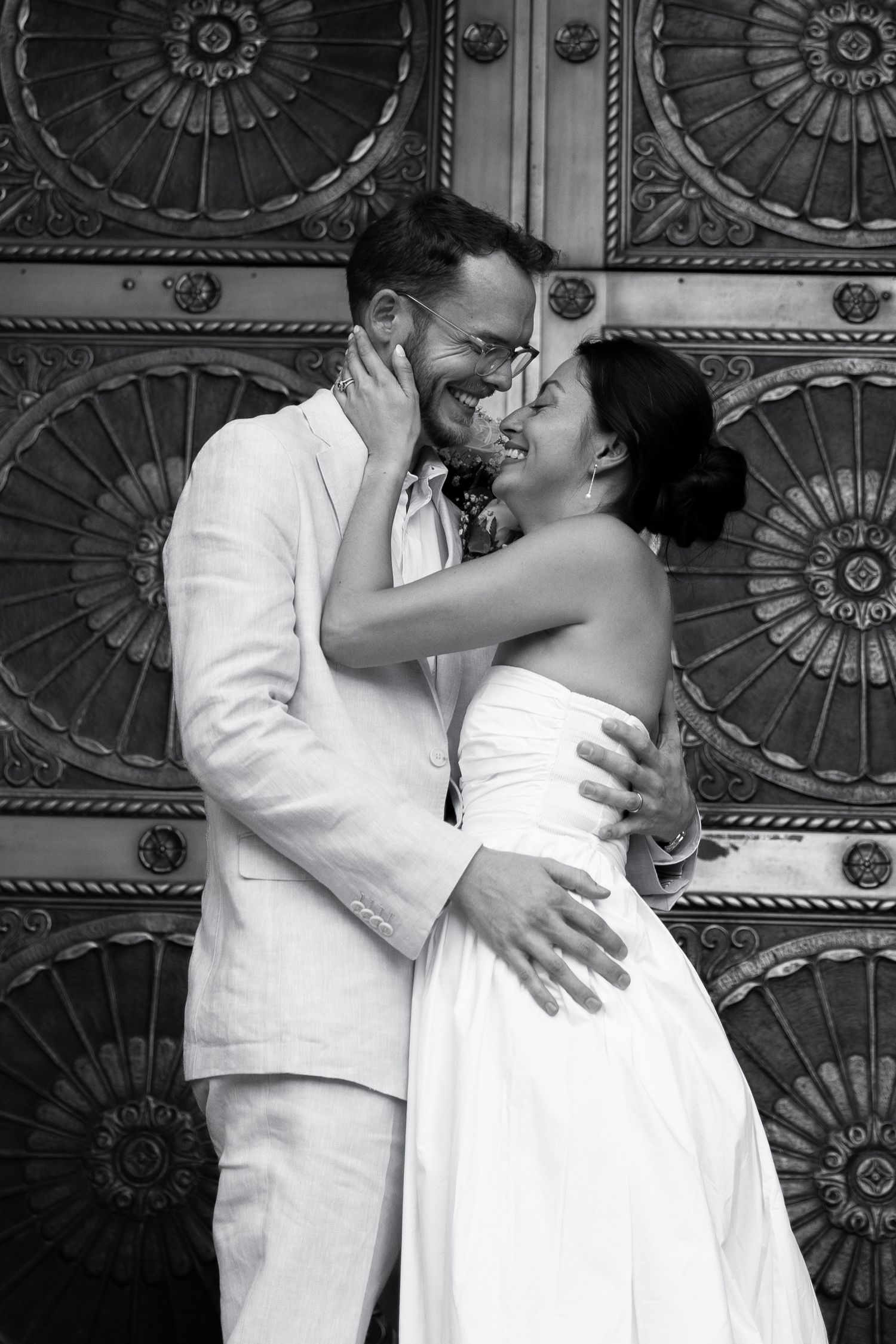 Black and white photo of smiling bride and groom embracing in front of decorative metal doors at Old Courthouse in Phoenix Arizona.