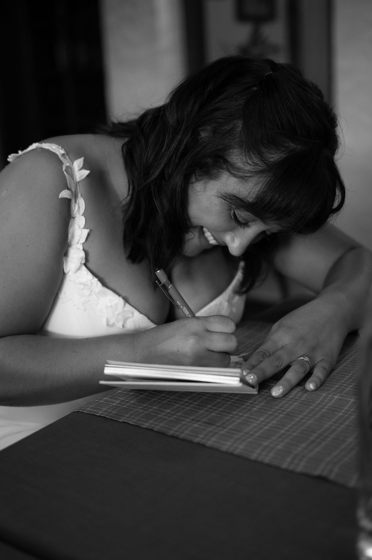 Bride in white lace dress smiles while writing in a notebook at a table in a black and white photo in Lauterbrunnen Switzerland.
