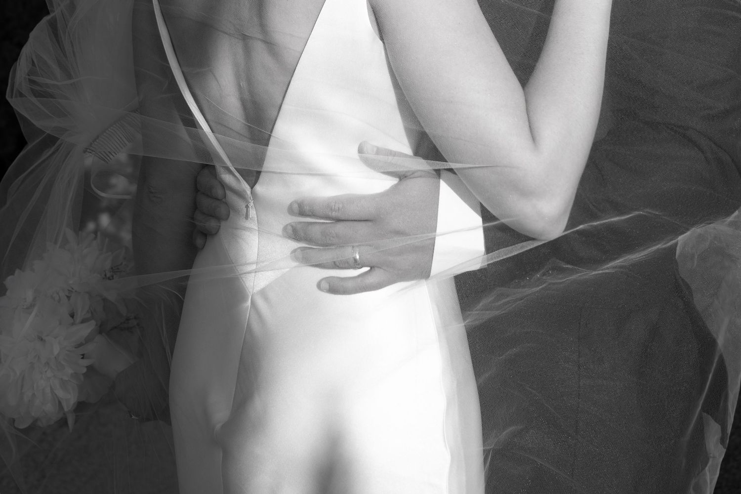 Black and white close-up of groom's hand on bride's waist showing wedding ring during first dance in Tuscany Italy.