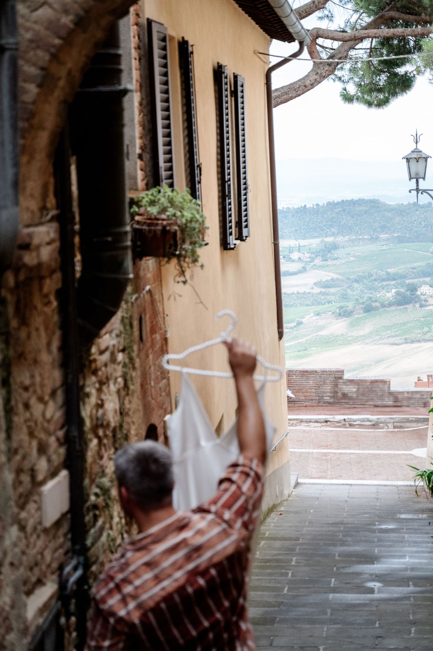 Man hanging a white wedding dress on a hook outside a charming Italian hillside village building in Tuscany Italy.