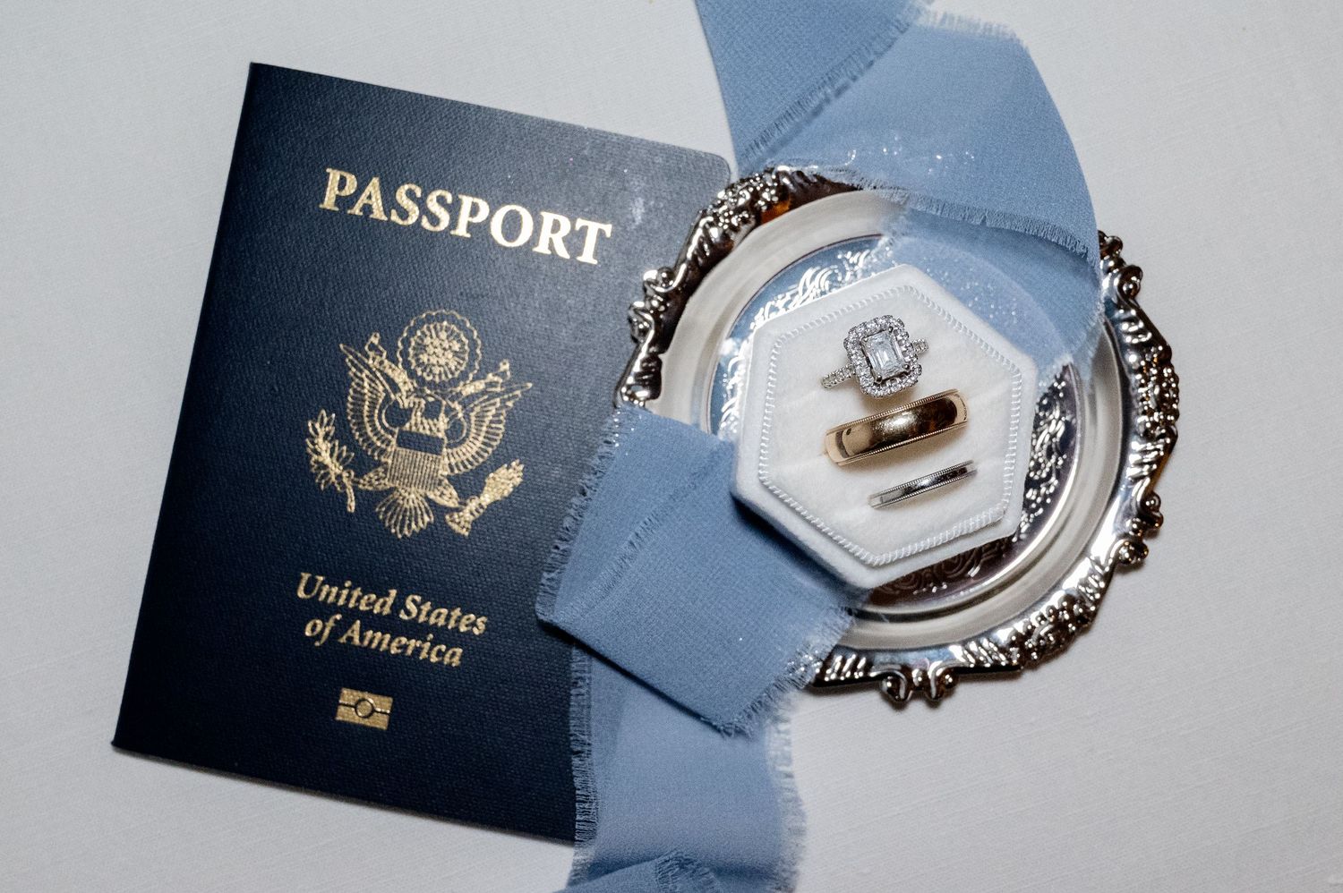 US passport with wedding rings on a blue ribbon and decorative plate, perfect for a destination wedding in Tuscany Italy.
