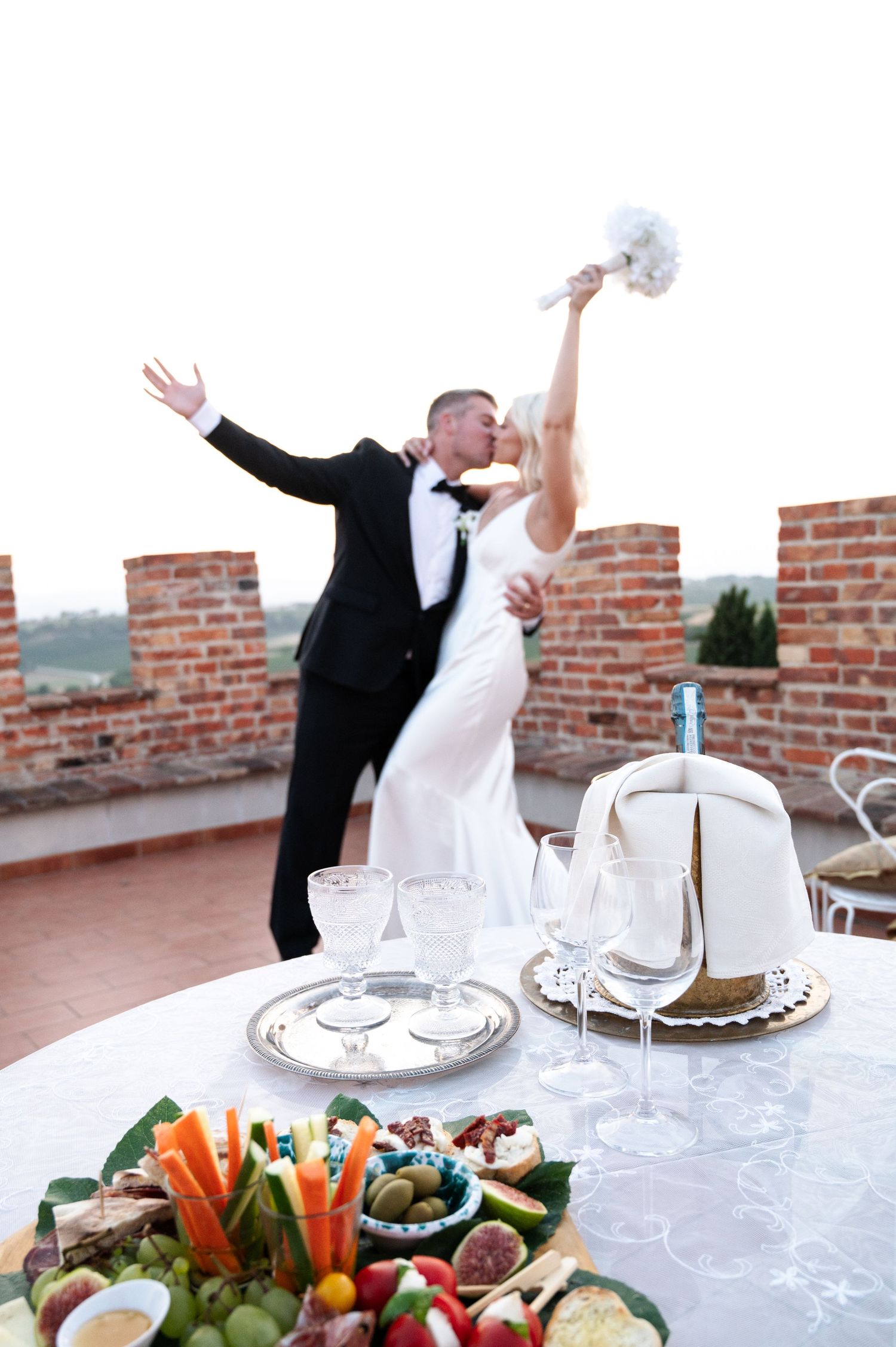 Bride and groom sharing a romantic kiss on a Tuscan rooftop terrace with a charcuterie table in foreground in Tuscany Italy.
