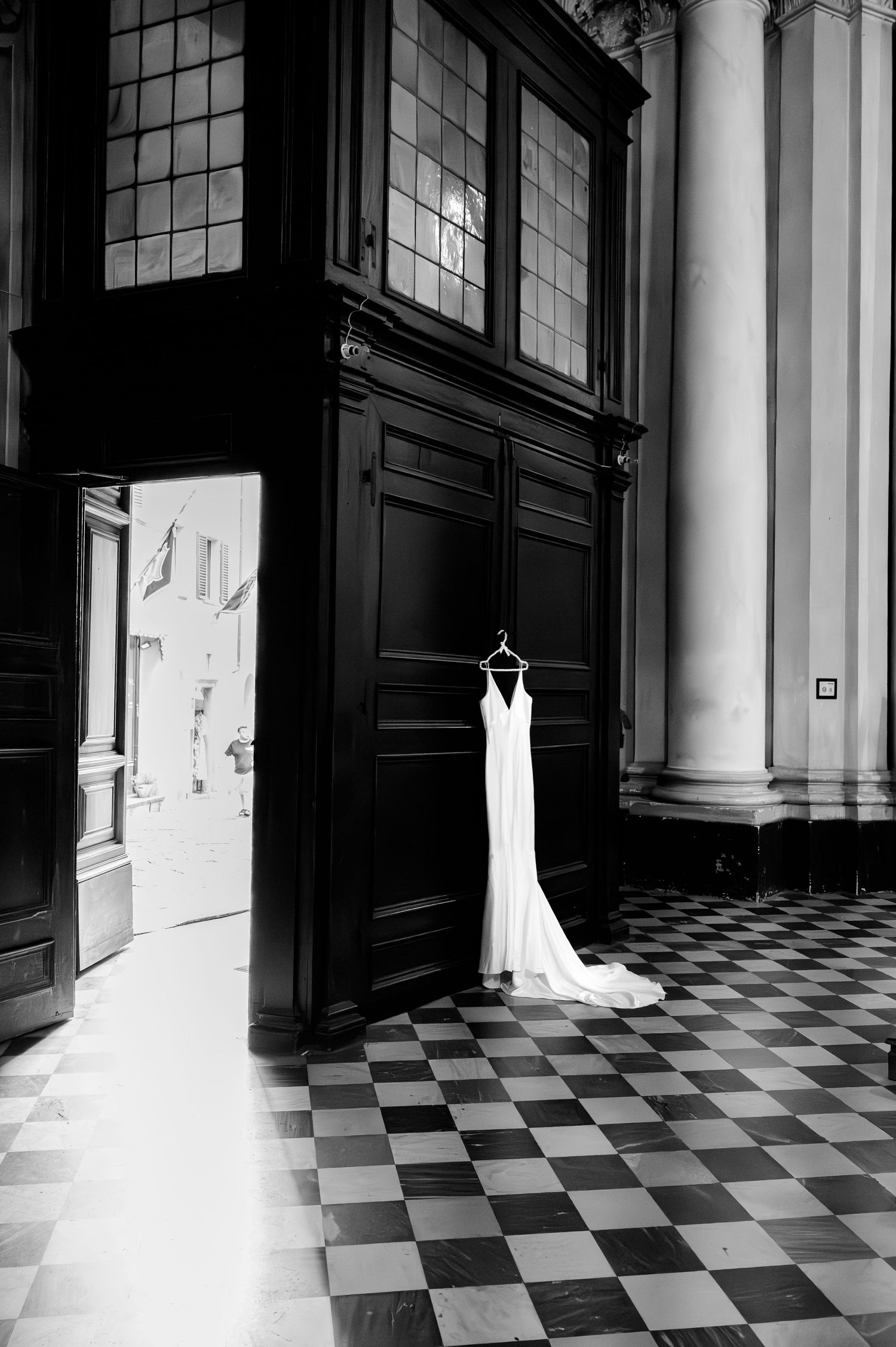 Black and white image of elegant wedding dress hanging in grand church interior with checkered marble floor in Tuscany Italy.