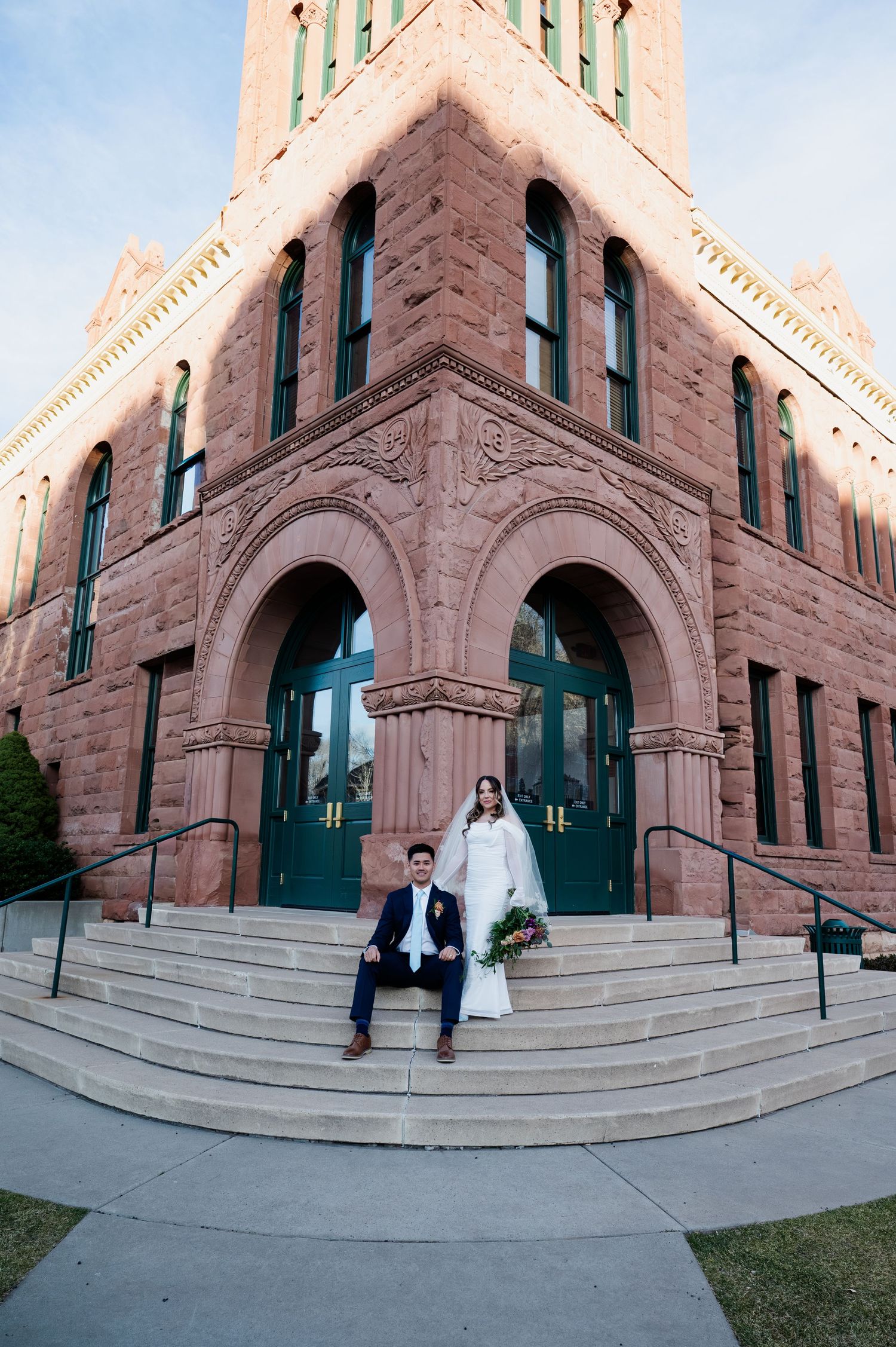 Wedding couple posing on steps of ornate red sandstone building at golden hour at the Flagstaff courthouse in Arizona.
