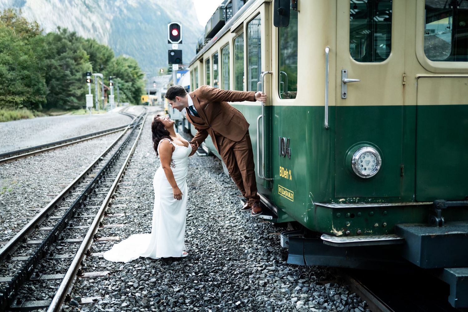 Bride and groom share romantic kiss beside vintage green Swiss mountain train at Lauterbrunnen station in Lauterbrunnen Switzerland.