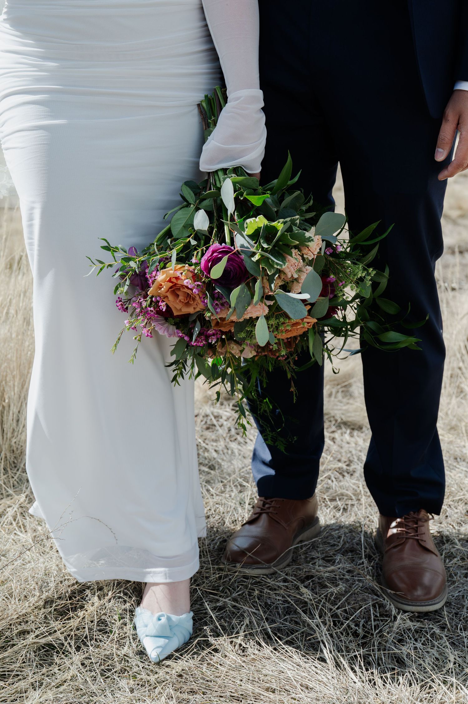 Close-up of bride in white gown with blue heels and groom holding lush wildflower wedding bouquet in Flagstaff Arizona.
