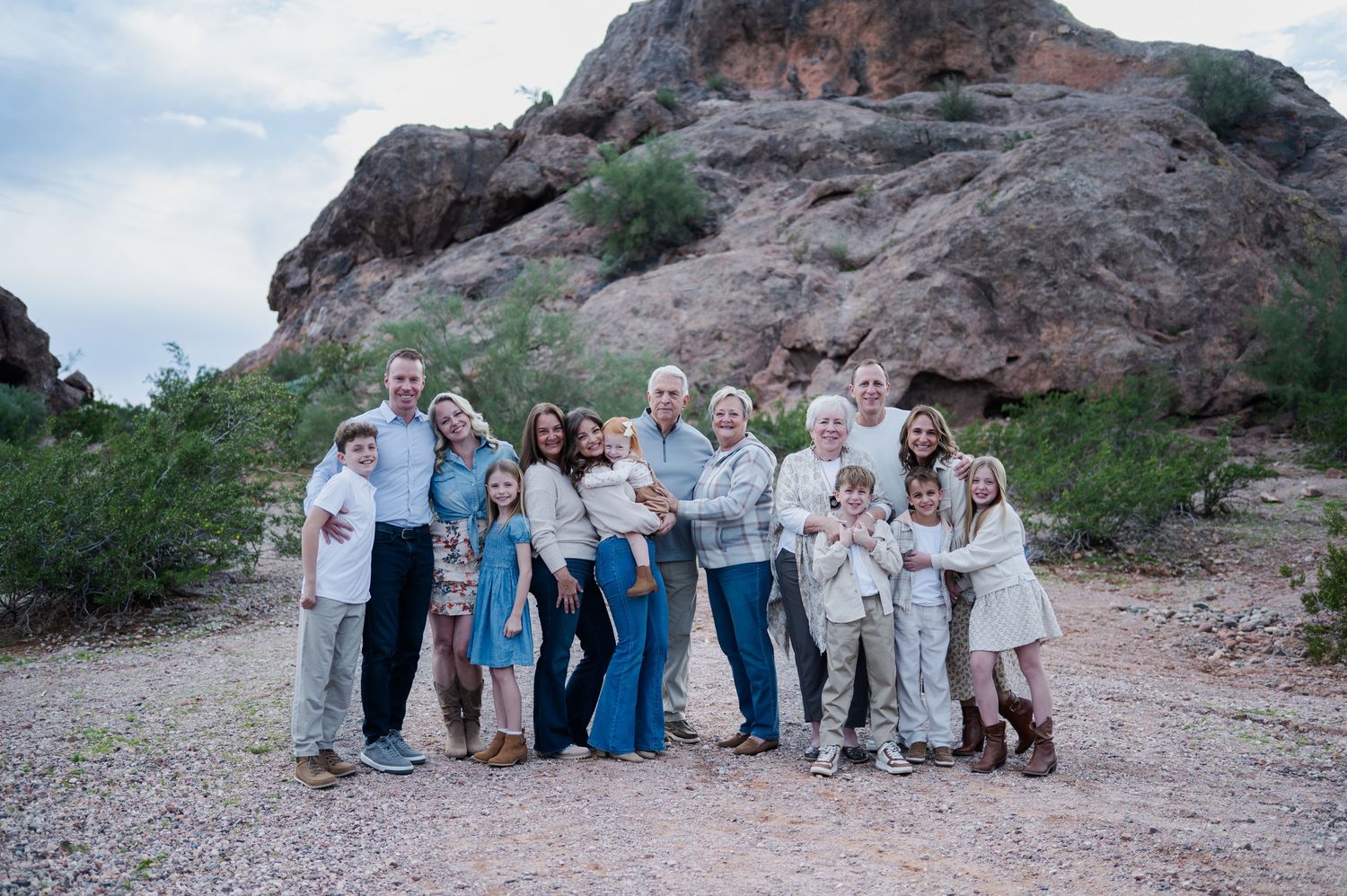 Large family group posing together outdoors in desert landscape with rocky mountain backdrop during family portrait session.