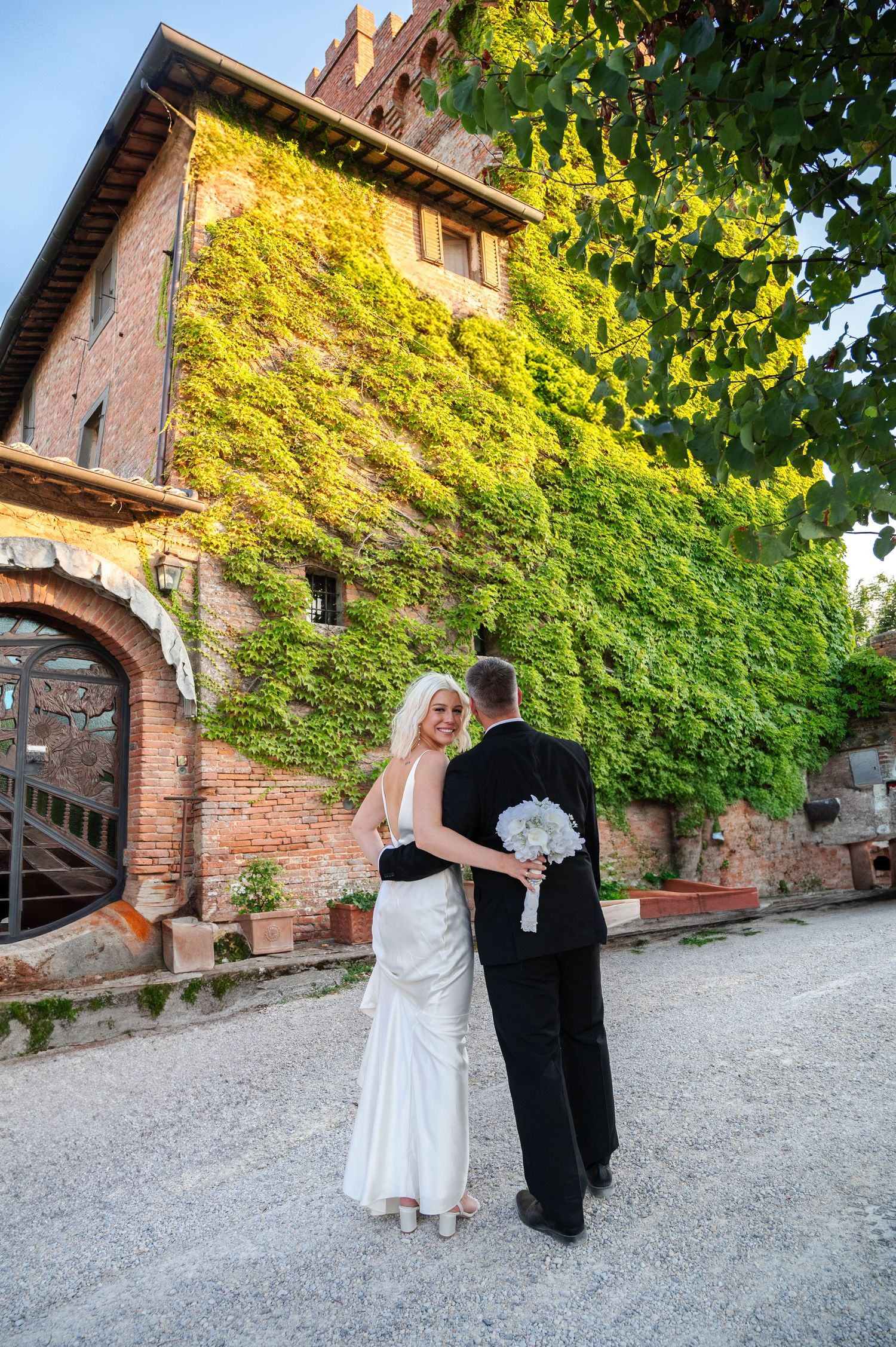 Bride and groom embracing before a stunning ivy-covered brick Tuscan villa on their wedding day in Tuscany Italy.