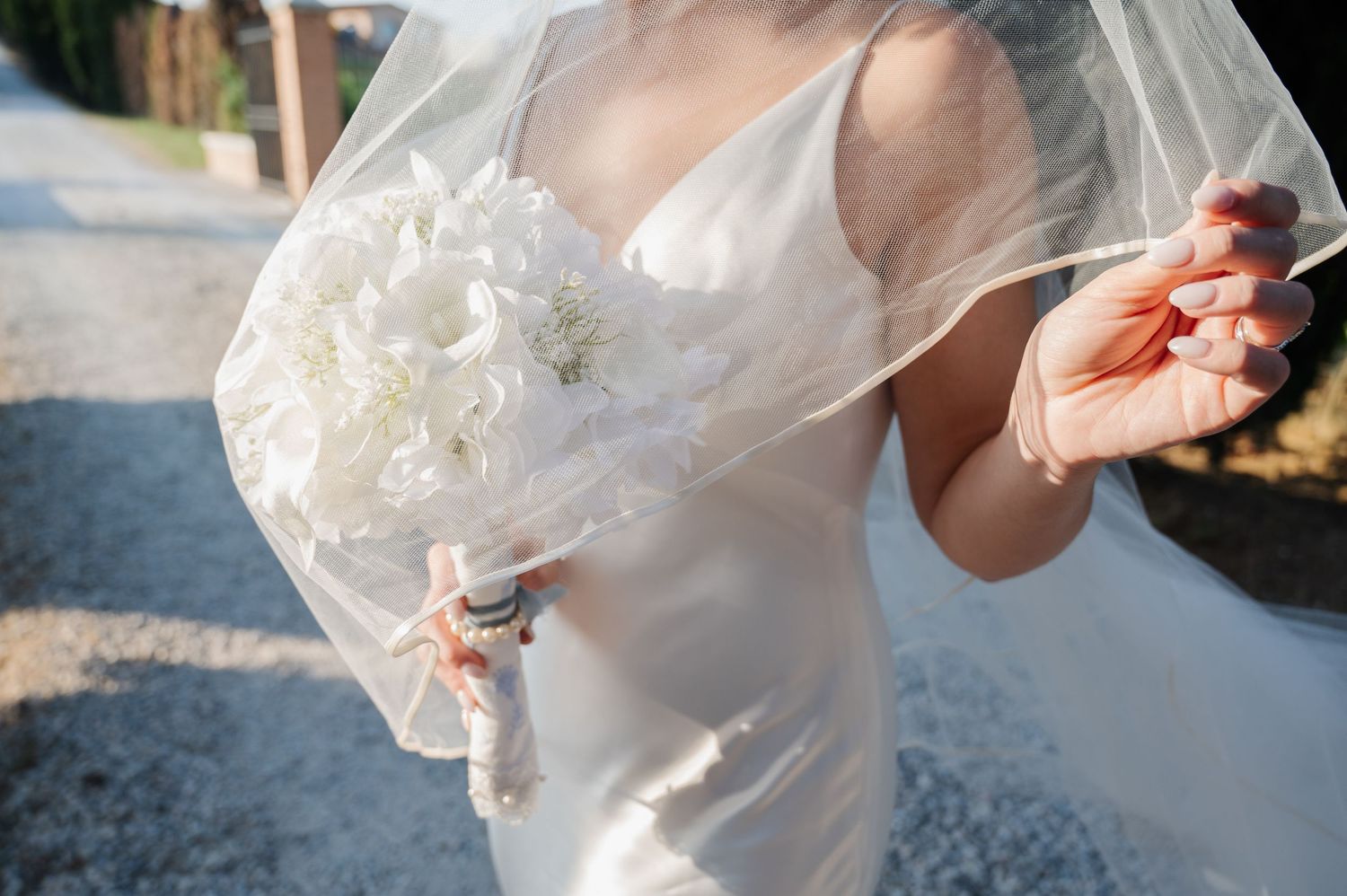 Close-up of bride holding a lush white floral bouquet with her flowing veil blowing in the breeze in Tuscany Italy.
