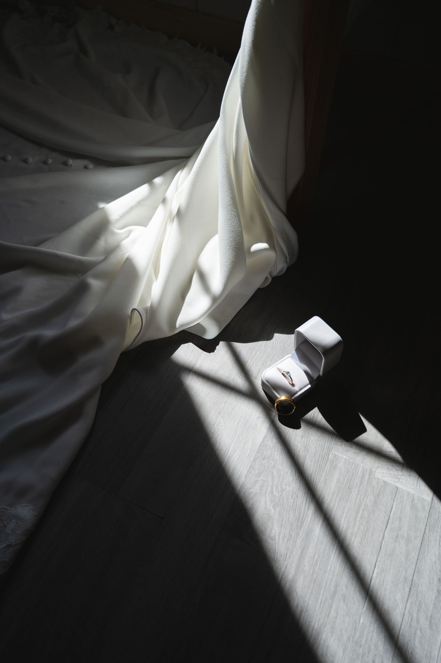 White wedding dress hem and bridal shoes casting dramatic shadows in sunlit dark room in Switzerland.