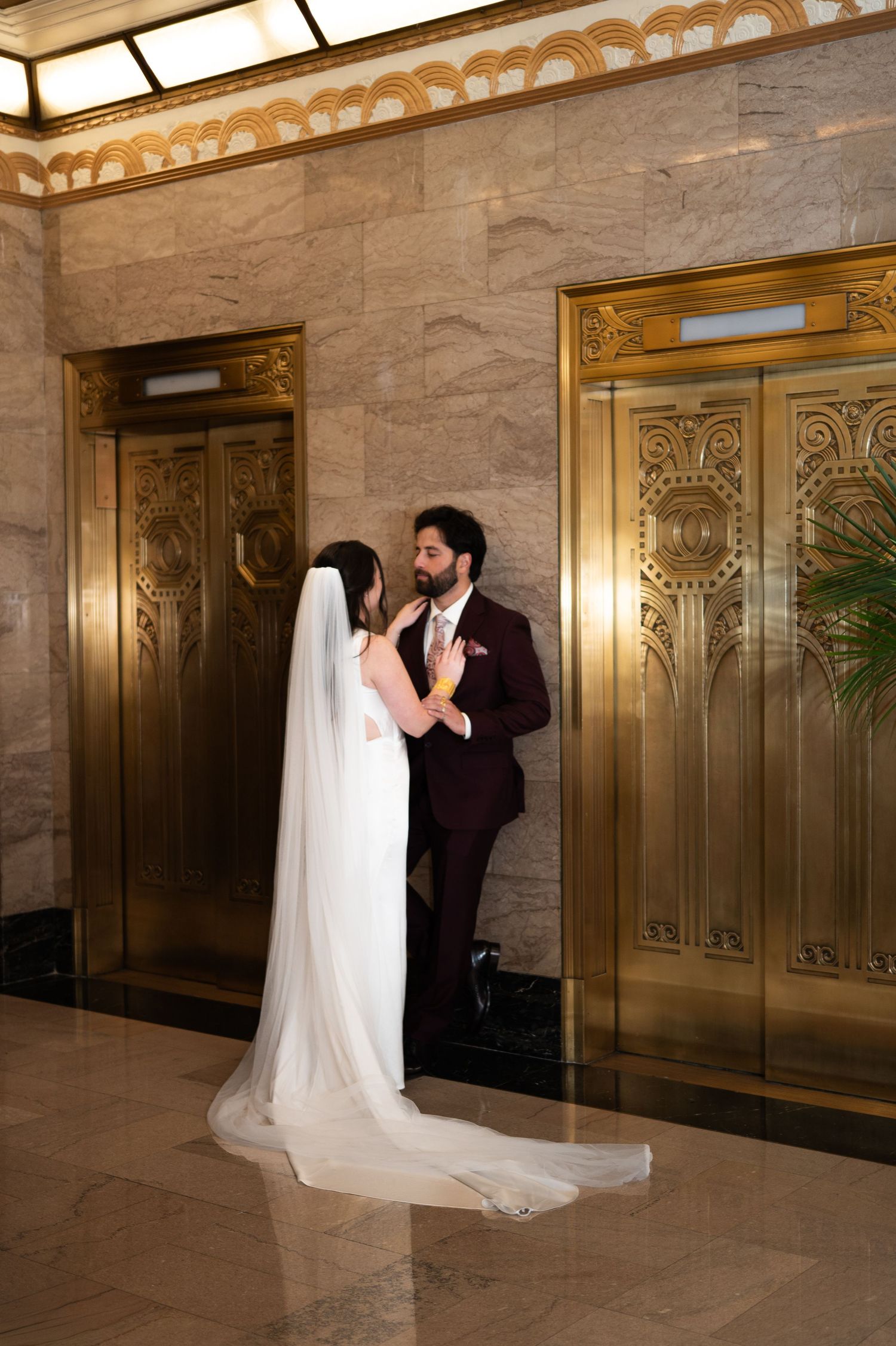 Bride and groom share intimate moment beside ornate gold elevator doors in elegant marble lobby at The Pendry Hotel in Chicago Illinois.