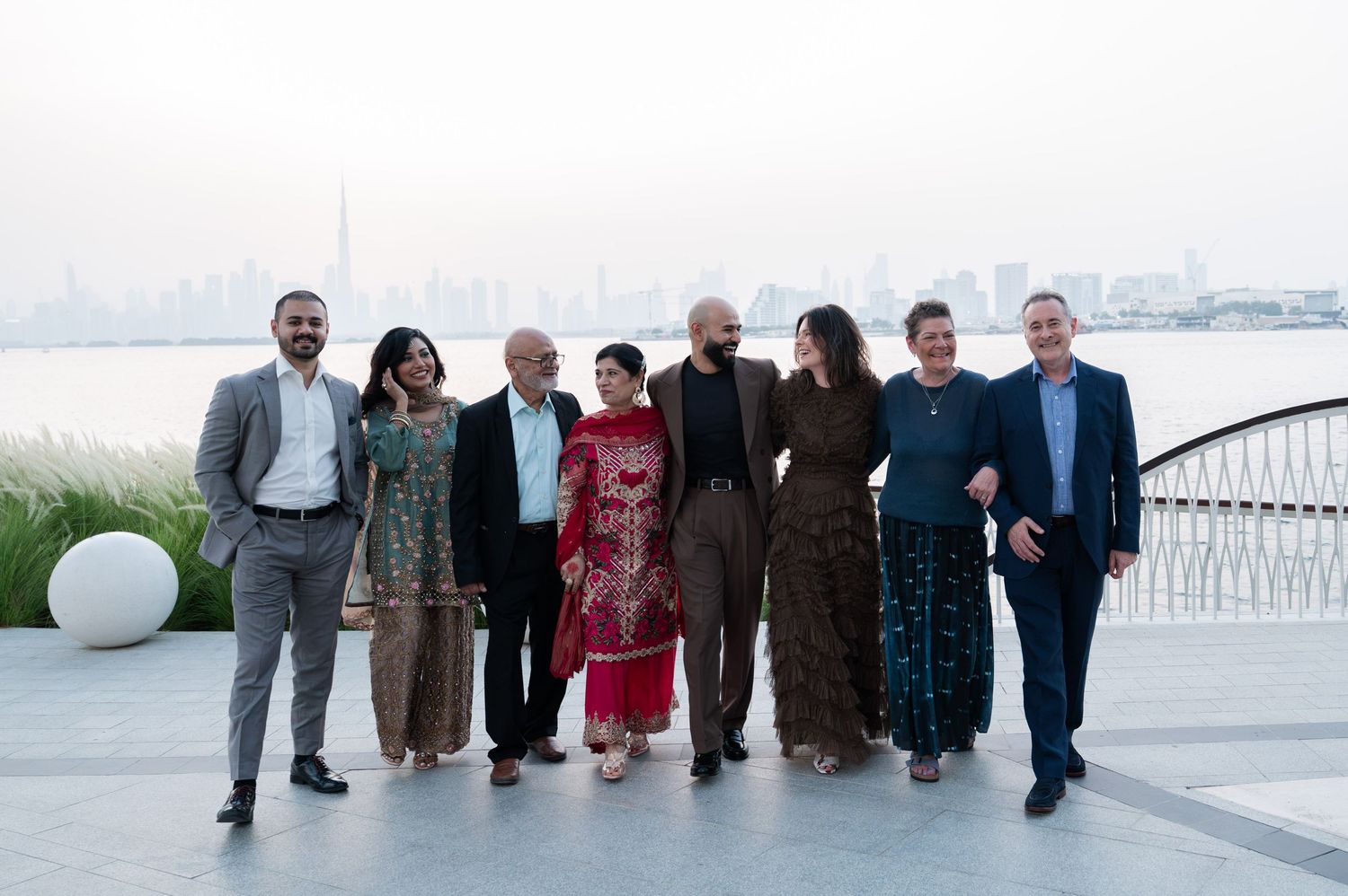 Group of eight professionals posing together outdoors by a waterfront with a city skyline at dusk.