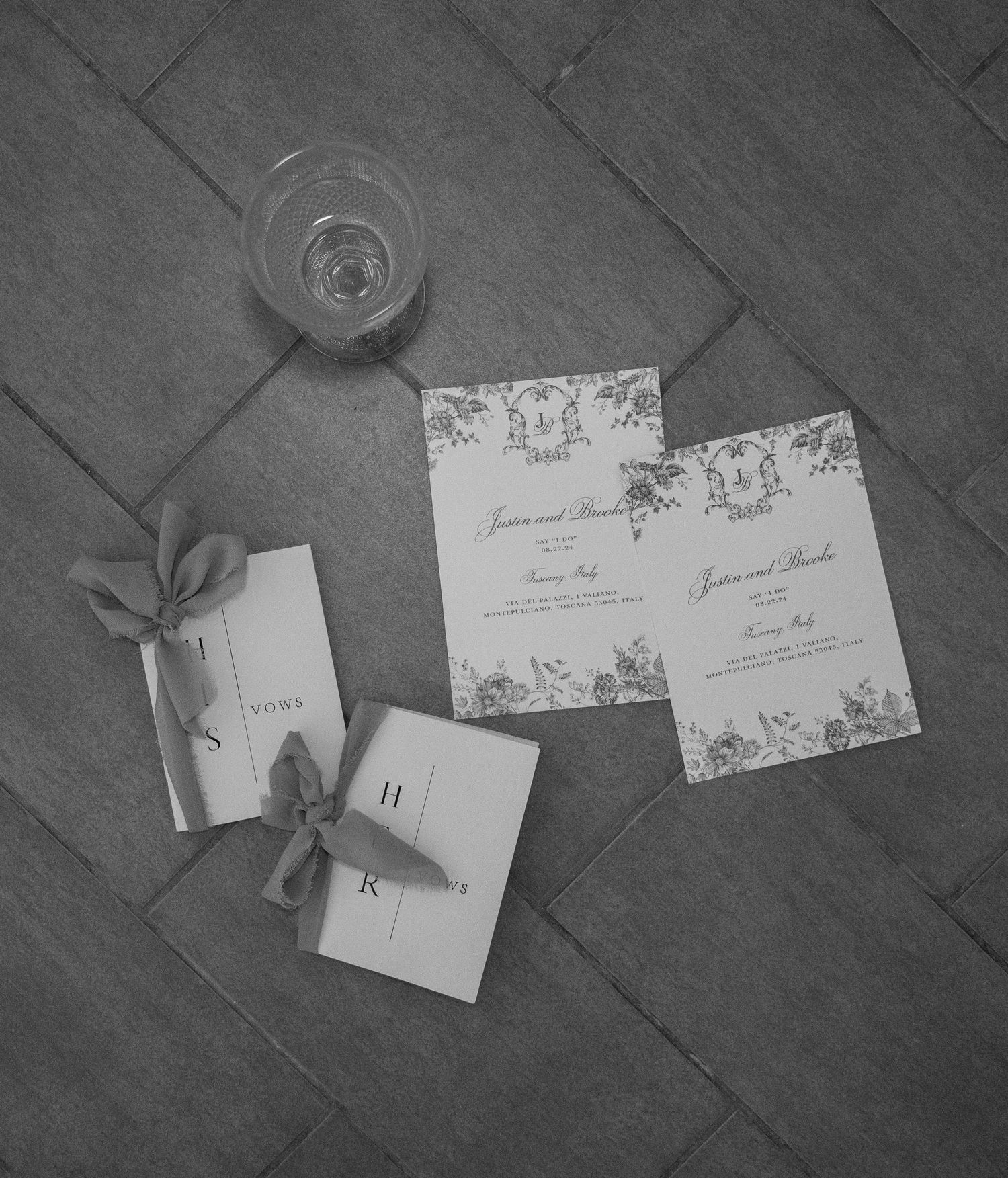 Black and white flat lay of elegant wedding stationery, invitations, and vow books on a tiled floor in Tuscany Italy.
