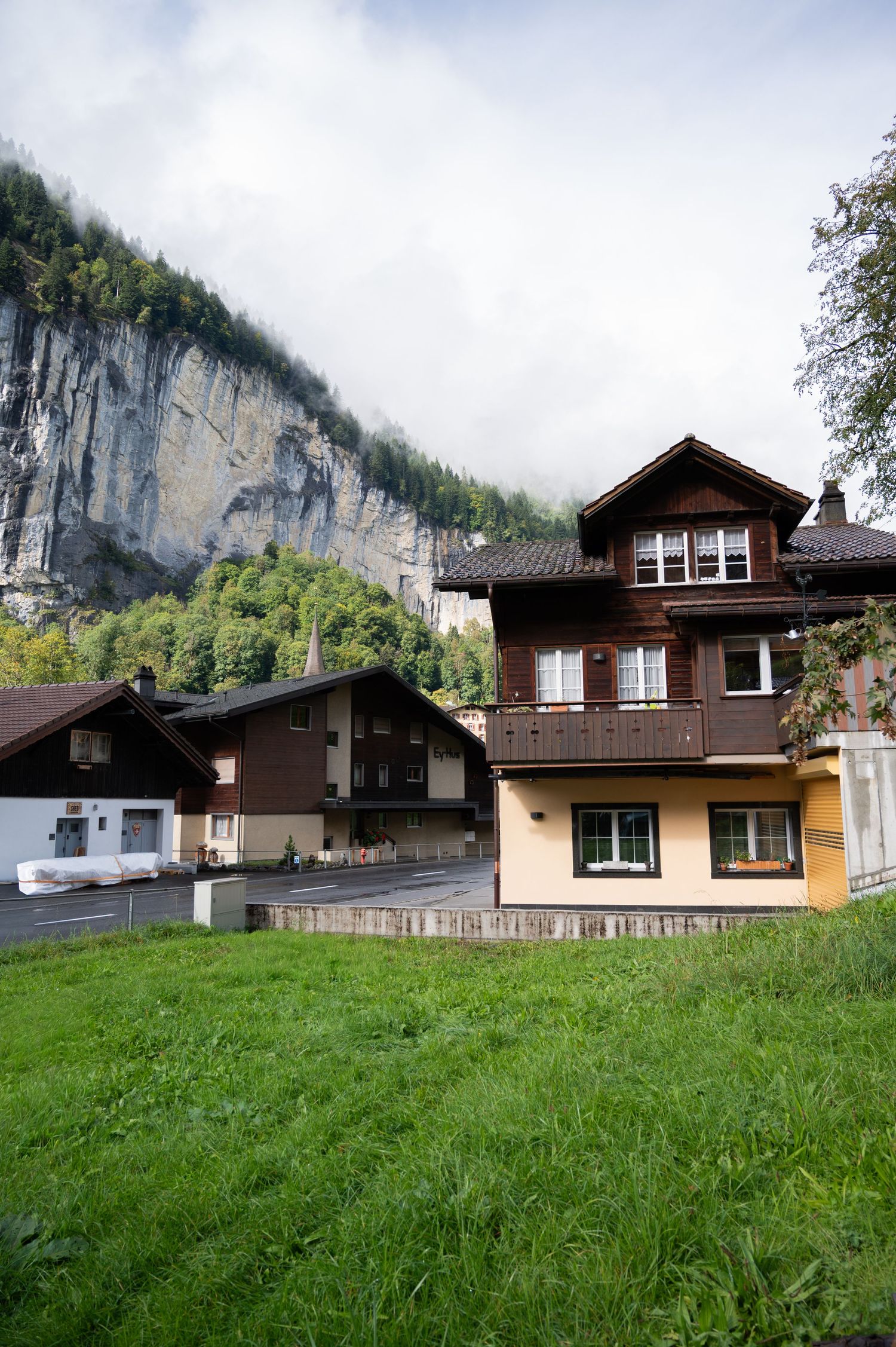 Traditional Swiss alpine chalets with wooden balconies nestled beneath dramatic misty limestone cliffs in Lauterbrunnen Switzerland.