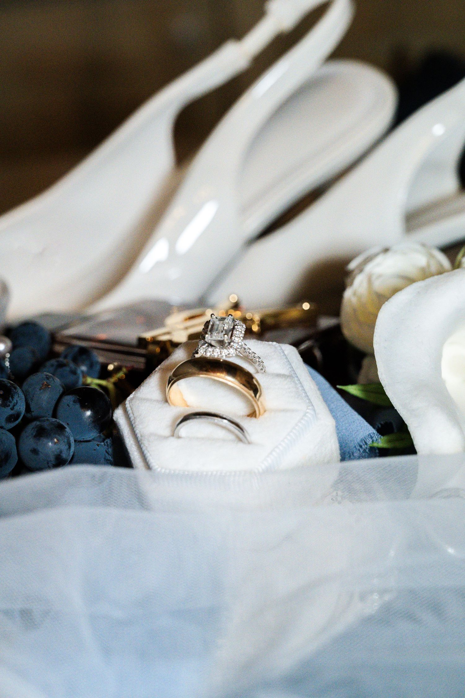 Wedding rings in a white velvet box surrounded by bridal accessories, shoes, and grapes in Tuscany Italy.