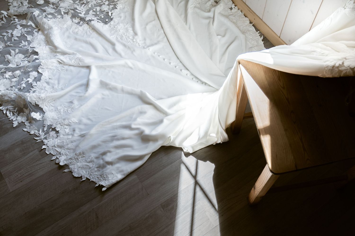 Elegant white lace wedding dress with floral appliques spread across a wooden floor in soft natural light in Switzerland.
