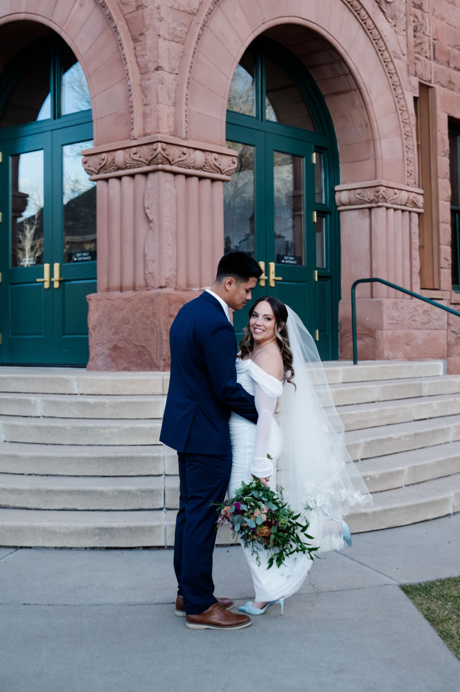 Smiling bride and groom embracing outside historic red sandstone church with teal doors at the Flagstaff courthouse in Arizona.