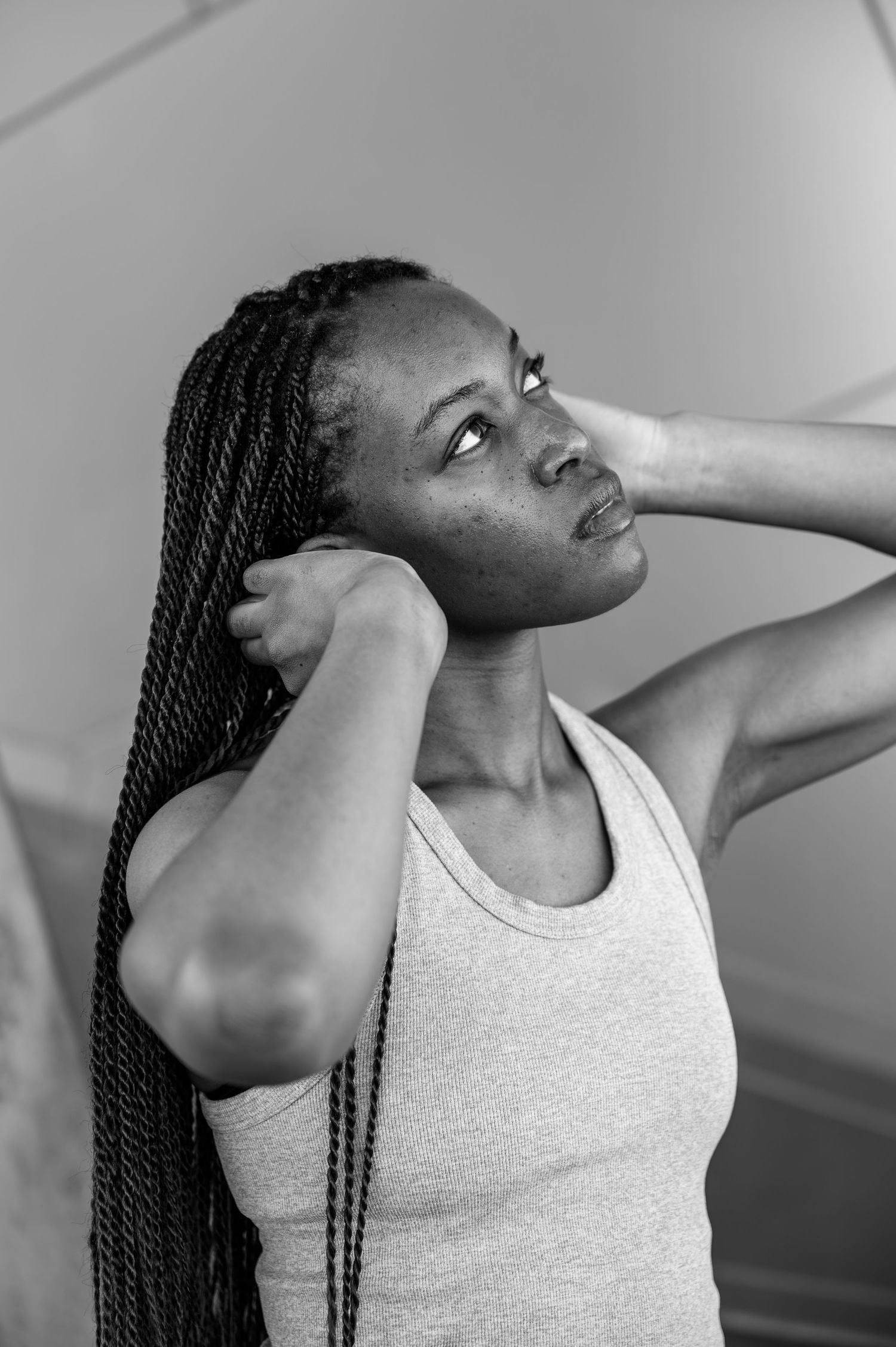 Black and white portrait of a woman with long braids holding her hair back and looking up.