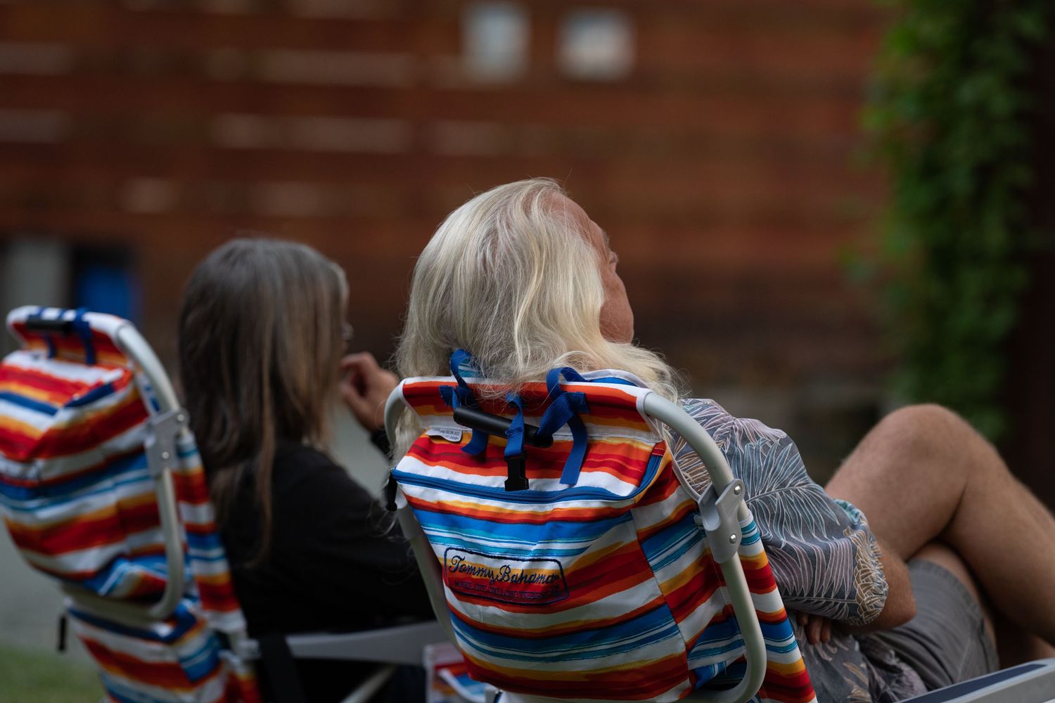 Two audience members in colorful striped folding lawn chairs watching an outdoor evening performance.