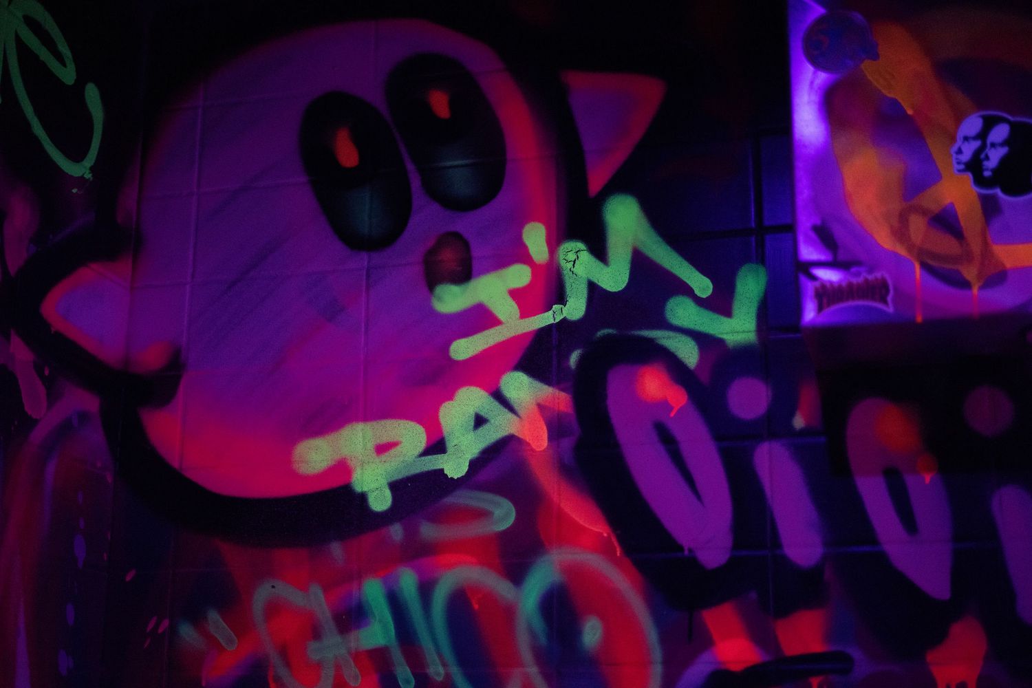 Neon UV graffiti art with pink cartoon character and green text on dark wall.
