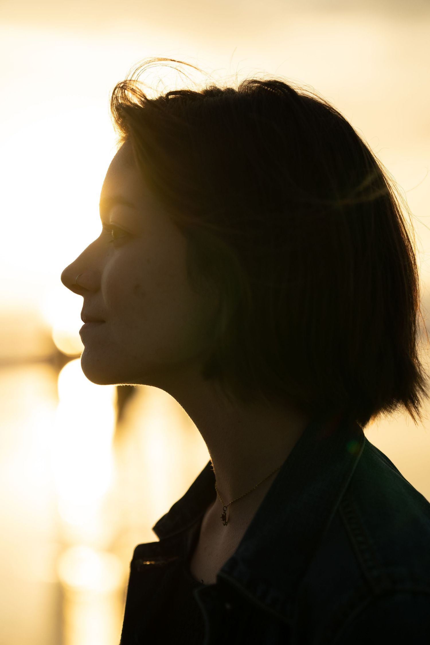 Silhouette of a young woman with short bob hair against a golden sunset backlight.