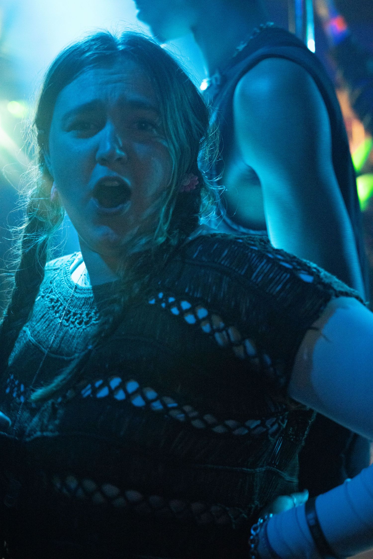 College age girl singing and dancing under blue stage lights at a club in London.
