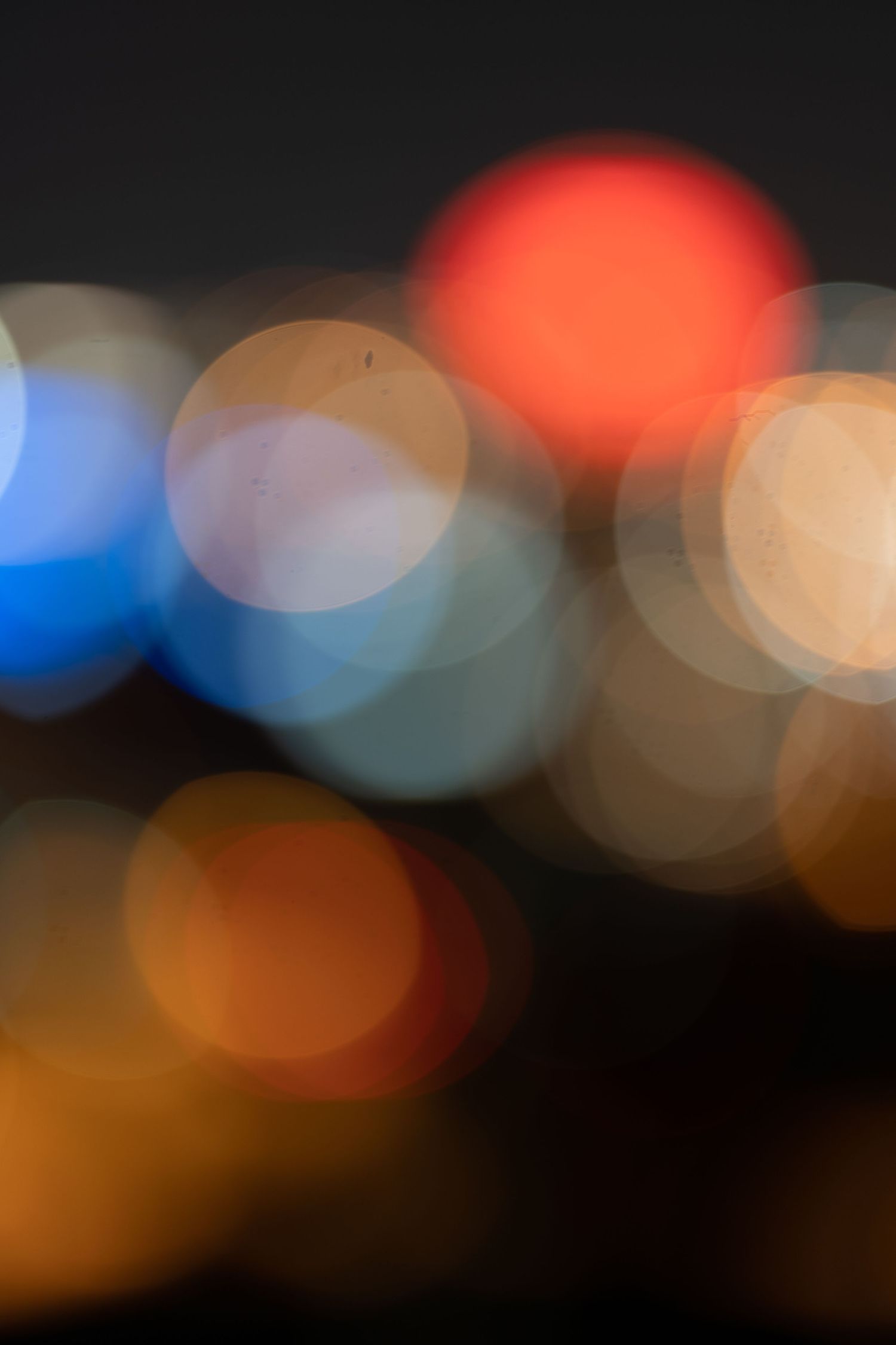 Colorful bokeh lights abstract background with red, blue, and orange circles against dark night sky.