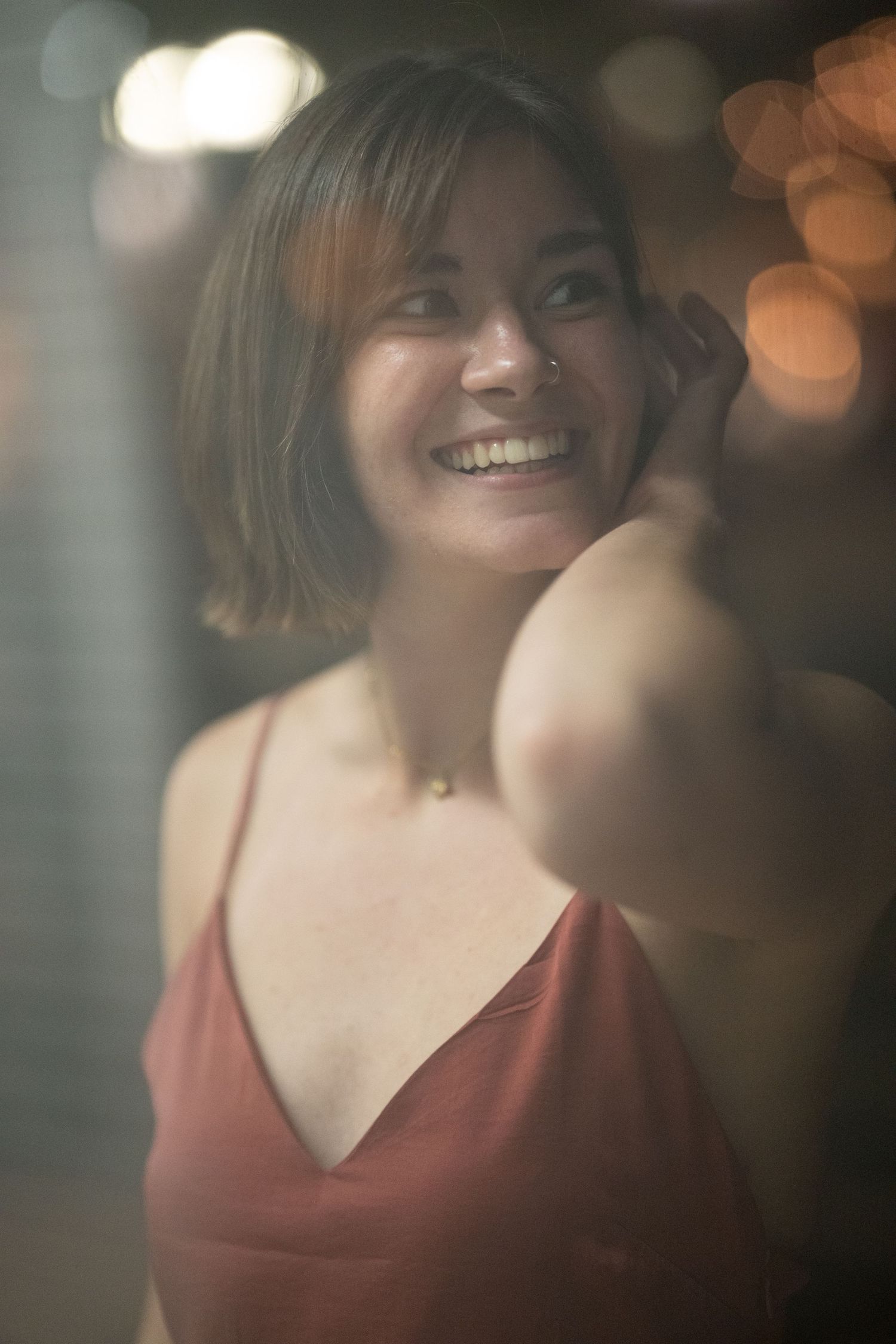Cheerful young woman with nose ring in red dress laughing with bokeh night lights behind her.