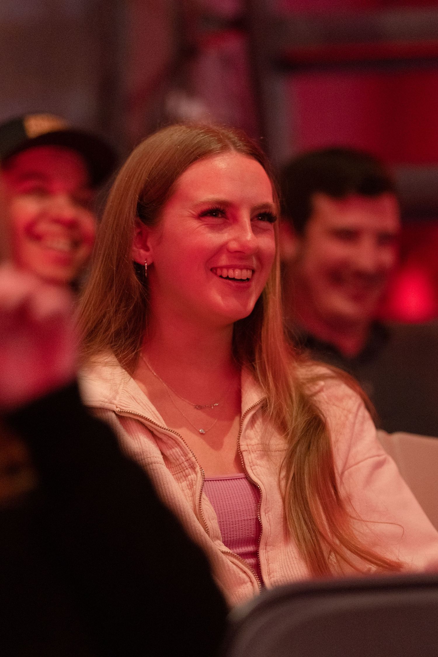 Young woman  with long blonde hair laughing and enjoying a live event under red ambient lighting.