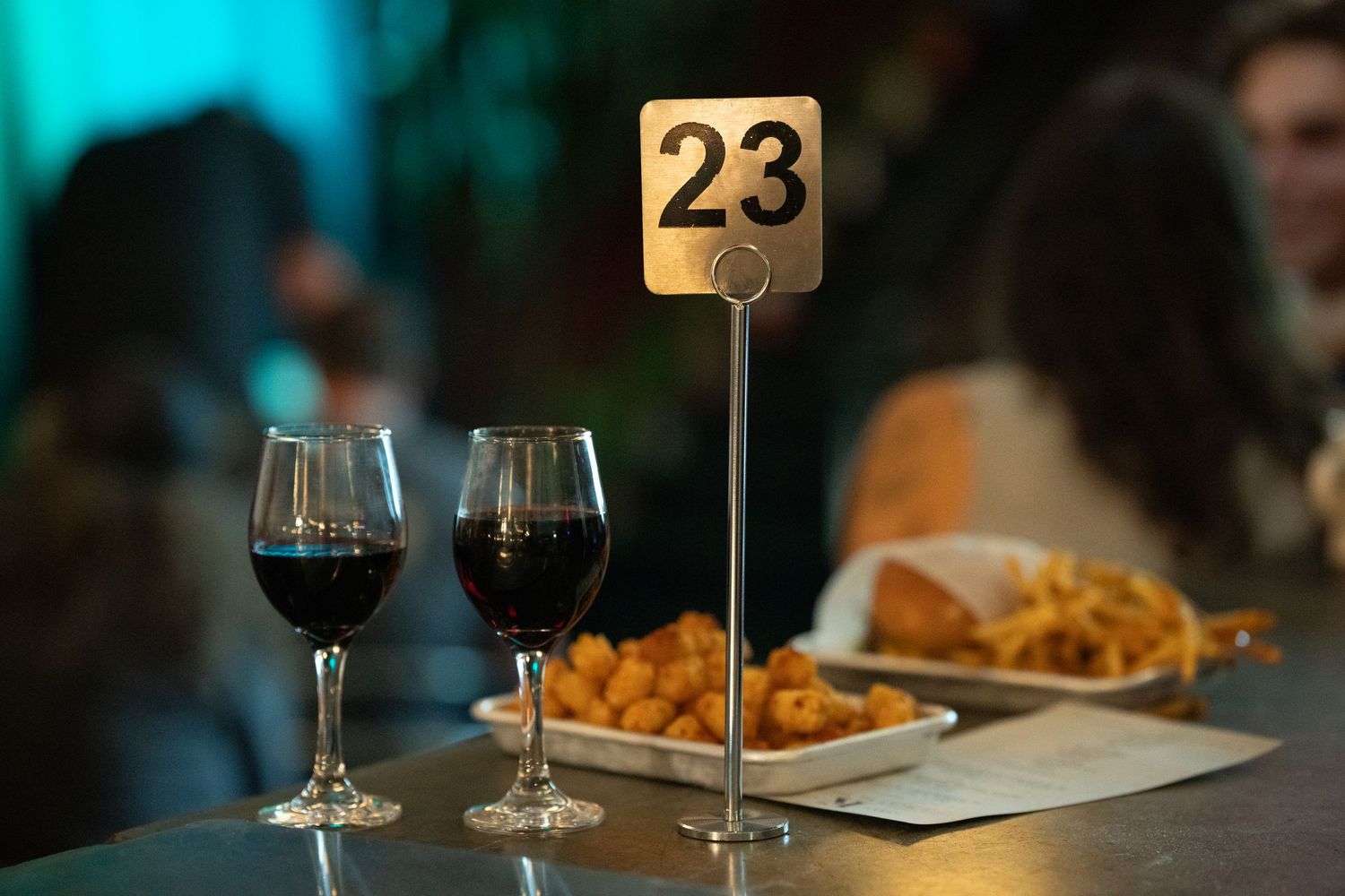 Two glasses of red wine beside table number 23 sign with appetizers at comedy show at Kreutzburg in San Luis Obispo, California