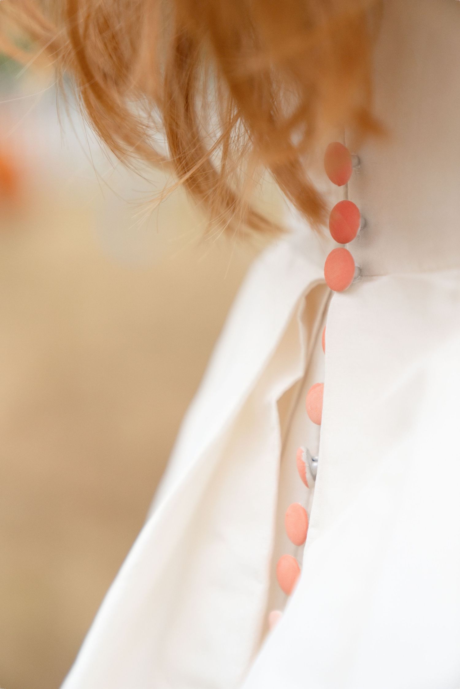 Close-up of white wedding dress back detail featuring delicate coral polka dot buttons on a redhead bride.