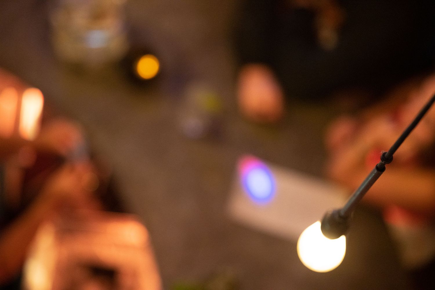 Glowing string light bulb in sharp focus against blurred warm bokeh party background at night.