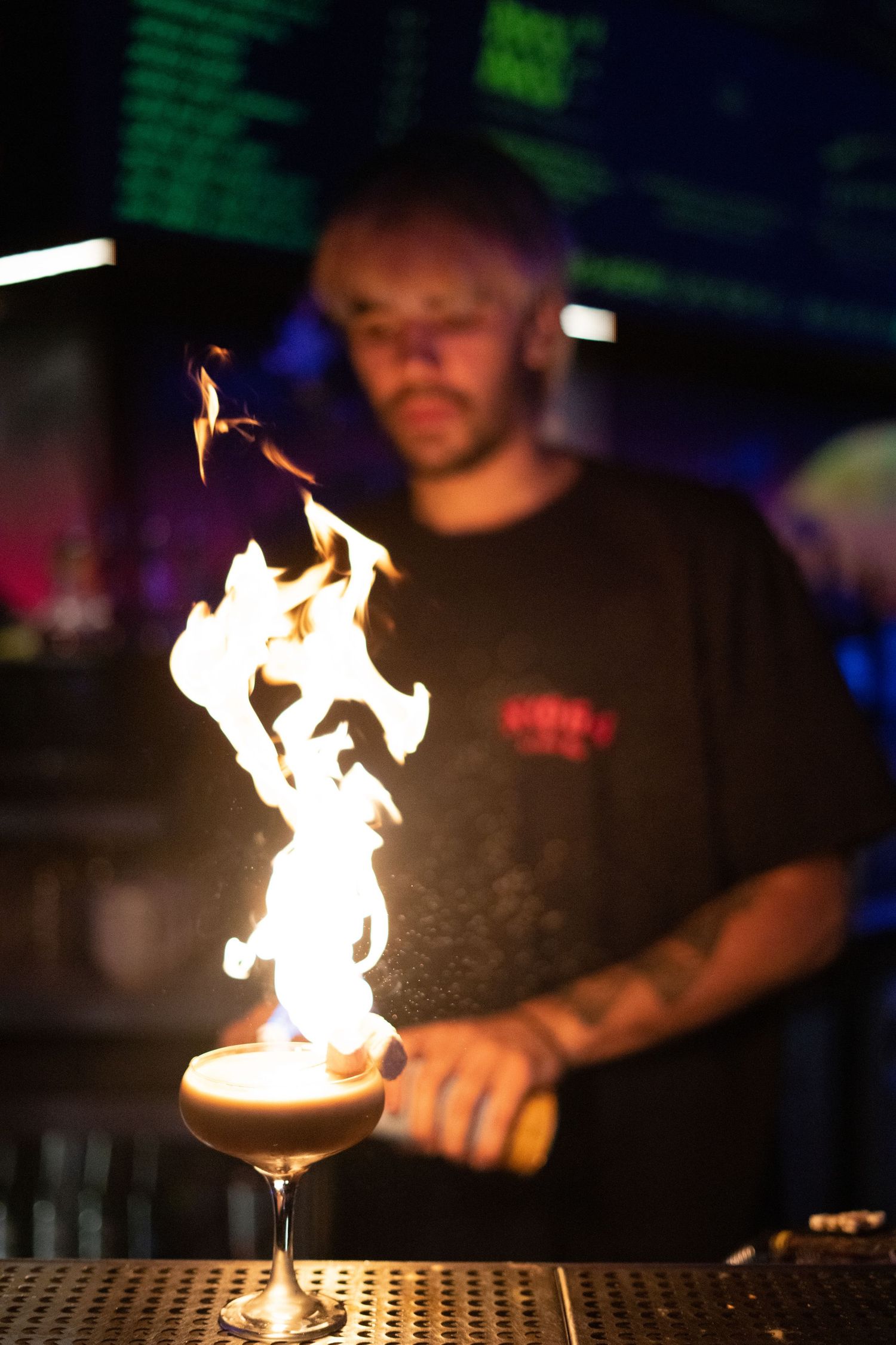 Bartender preparing a flaming cocktail with dramatic fire flames at a nightclub bar.