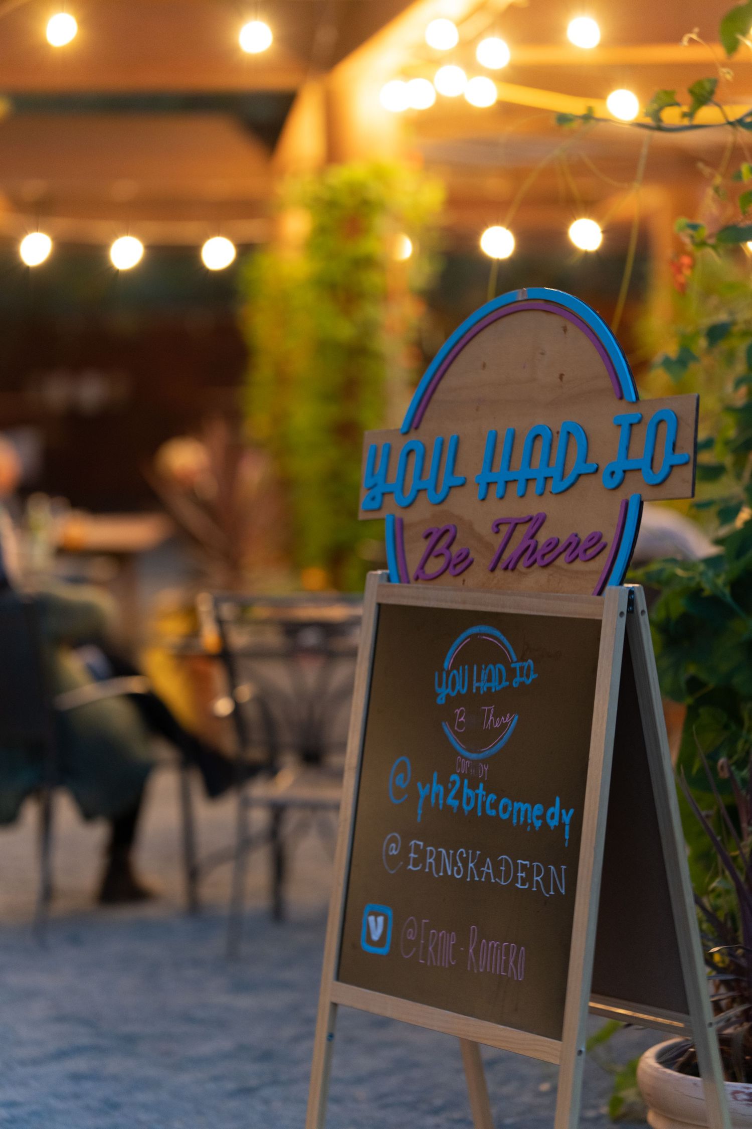 You Had To Be There comedy show sandwich board sign with neon logo and social media handles at outdoor venue.