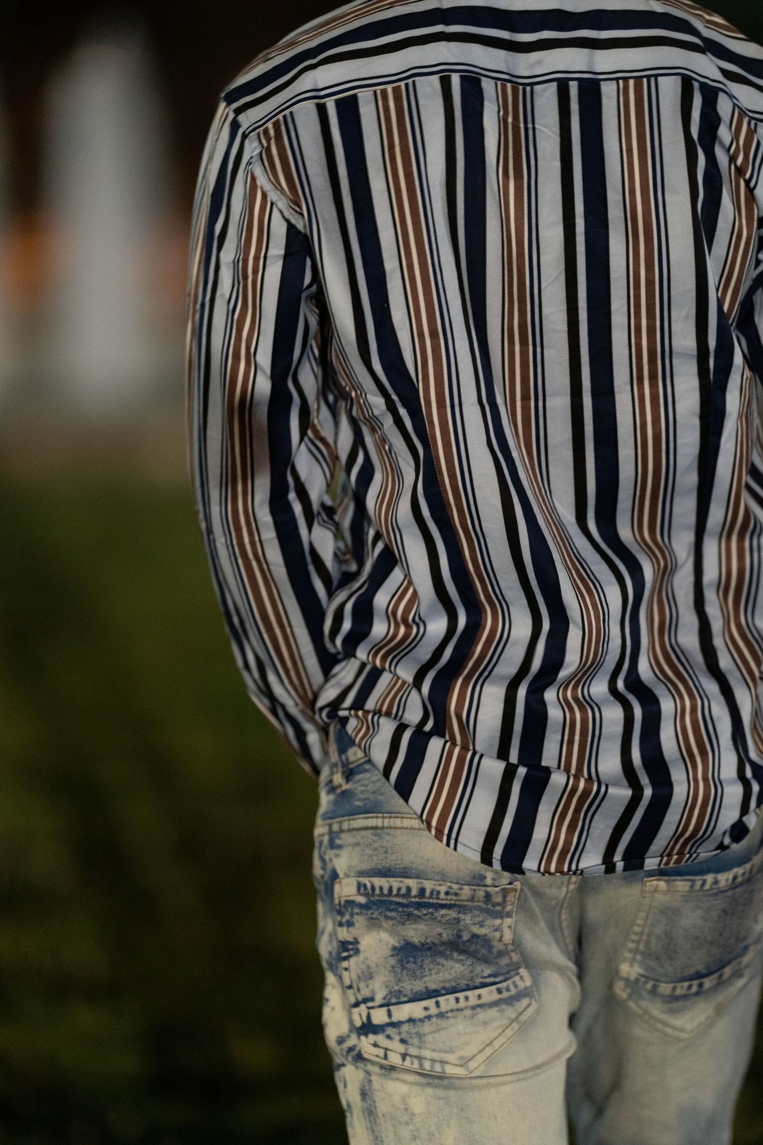 Back view of person wearing striped shirt and light blue distressed denim jeans outdoors.