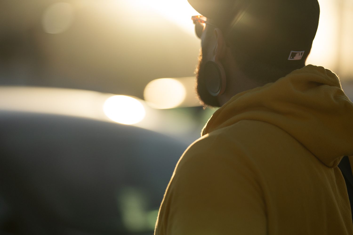 Man in yellow hoodie and cap standing backlit by golden sunset light outdoors.