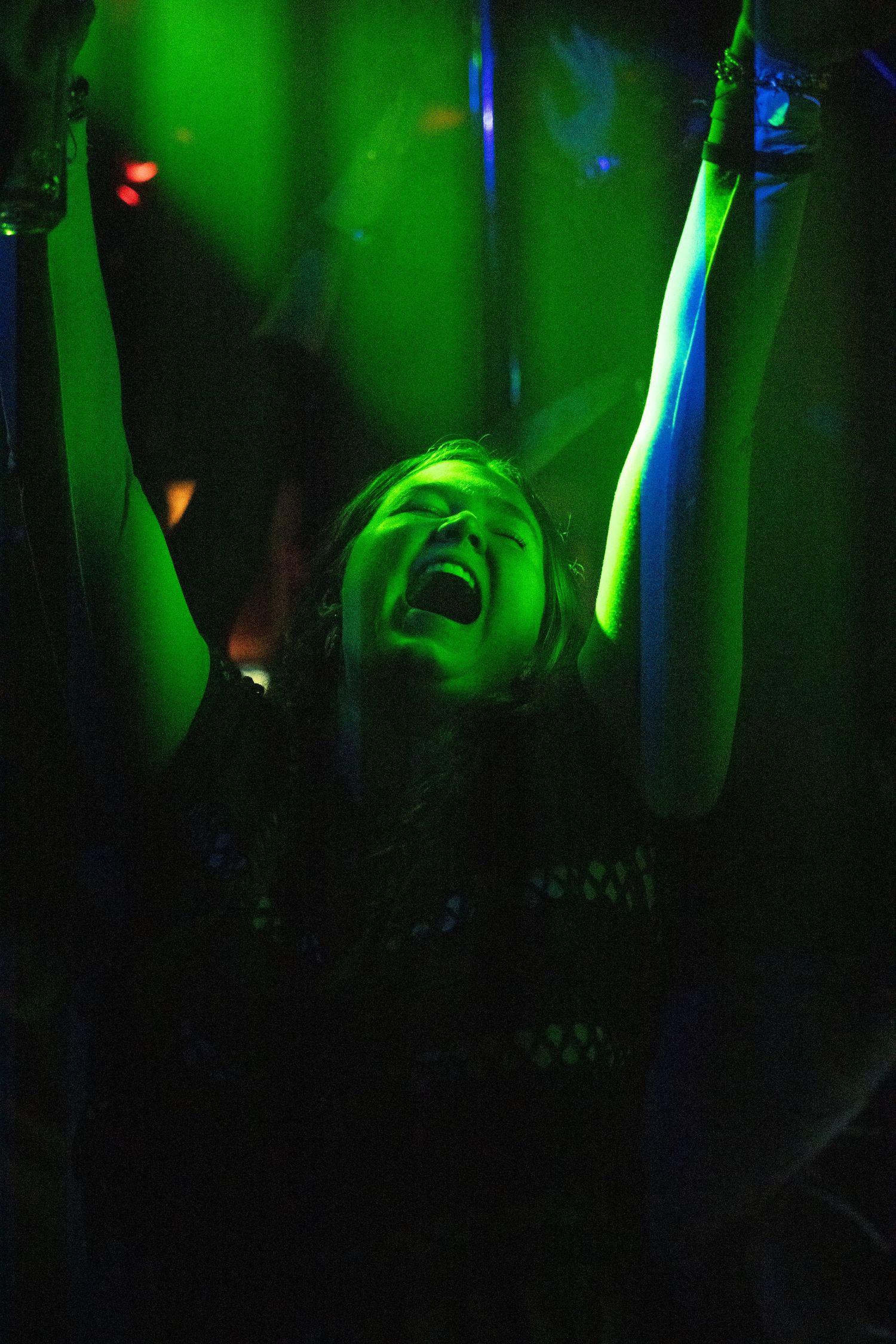 Woman with arms raised dancing under green stage lights at a nightclub in London.