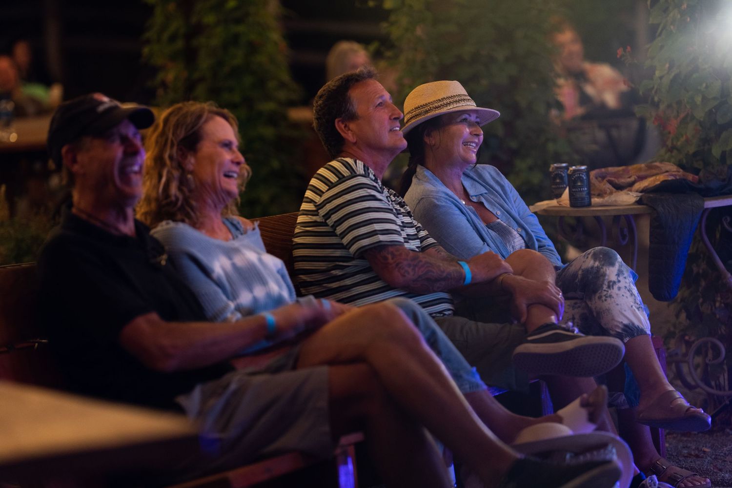 Group of five adults laughing and enjoying an outdoor comedy show seated together at a nighttime event.