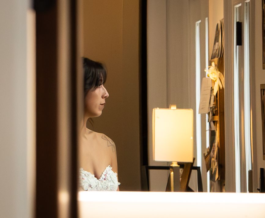 A woman in a white lace dress gazes at artwork in an elegantly lit gallery room.