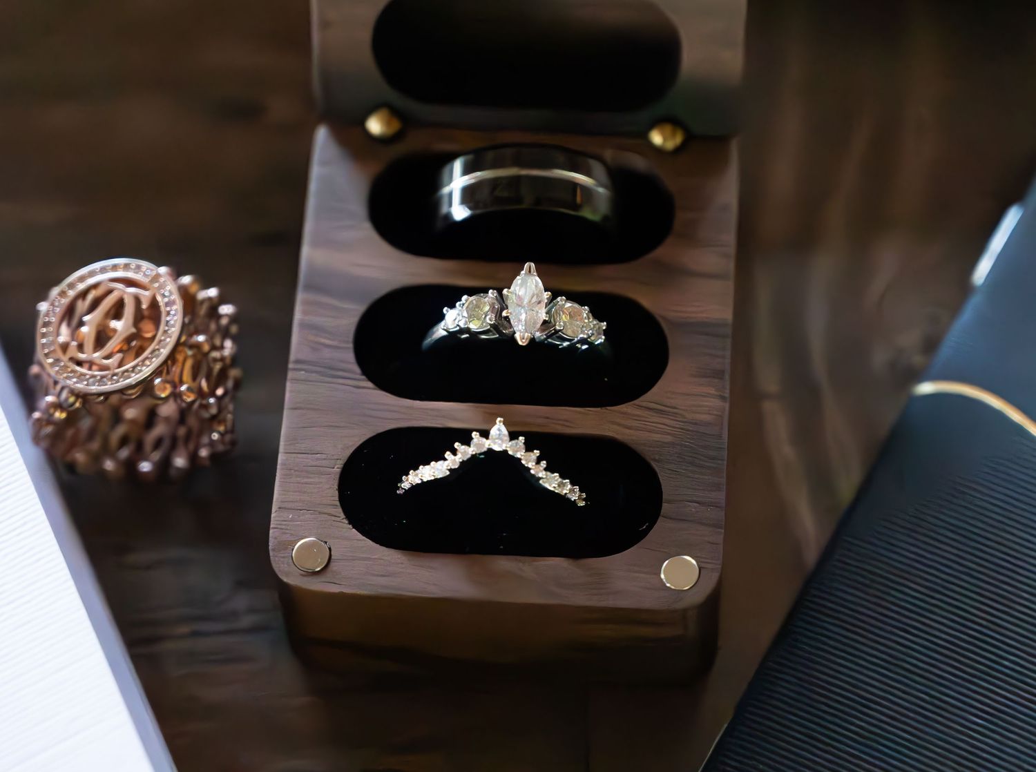 Elegant wedding rings displayed in a walnut wood ring box with black velvet slots, featuring diamond and gold bands.