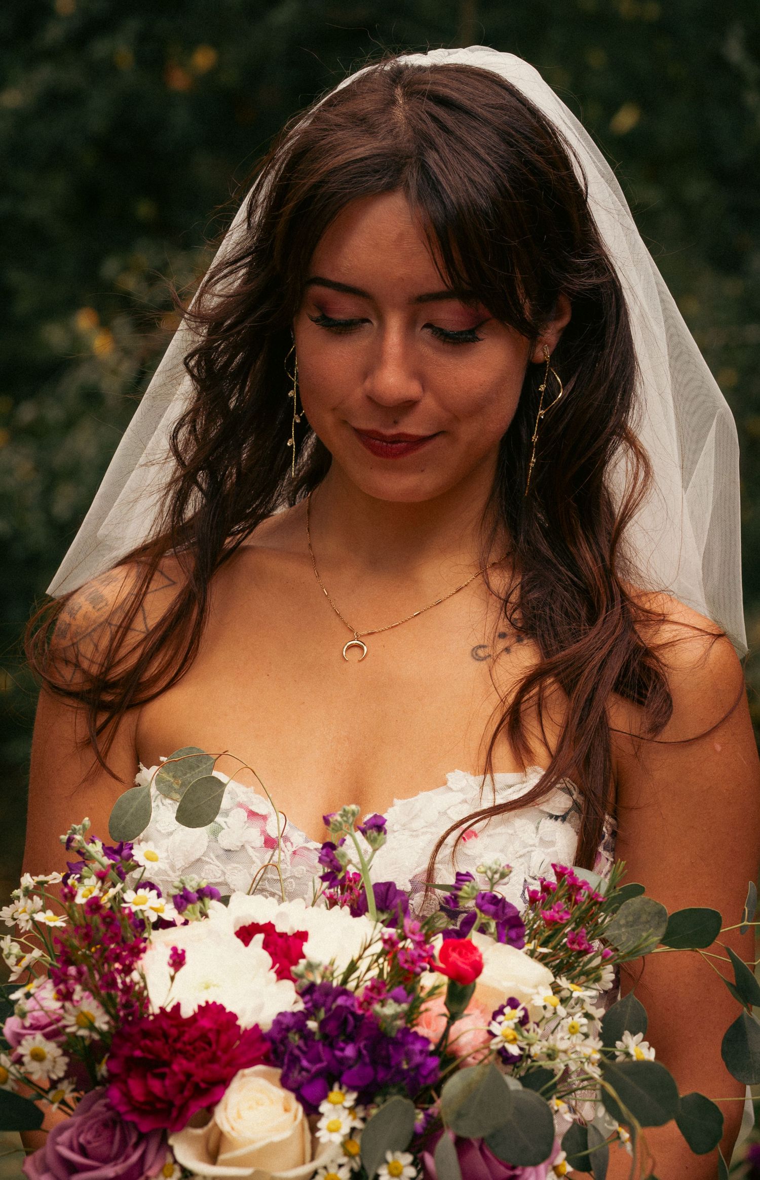 Bride in white veil looking down at colorful purple and pink wedding bouquet.