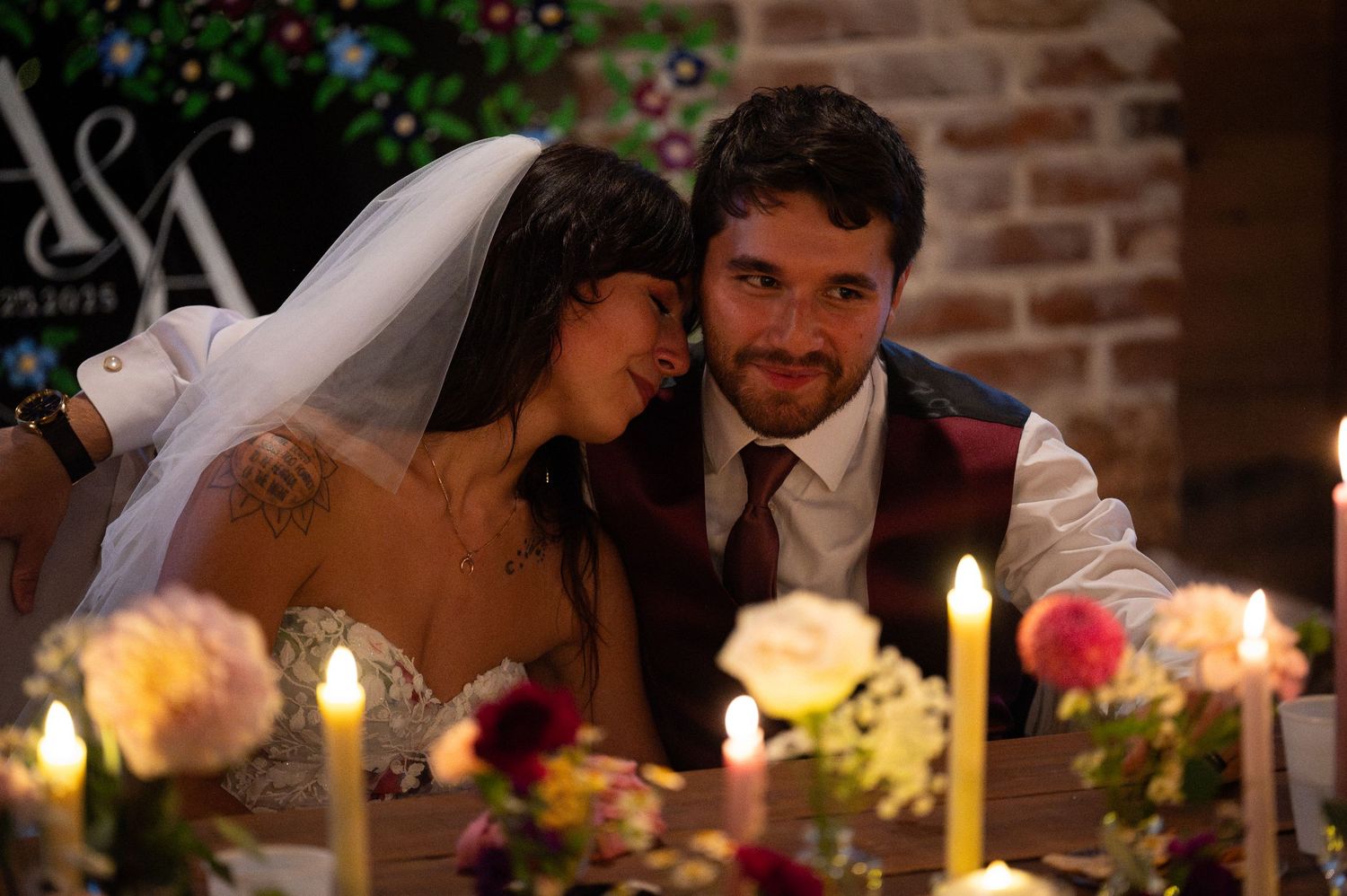 Bride and groom share a romantic candlelit moment at their wedding reception table adorned with flowers and candles.