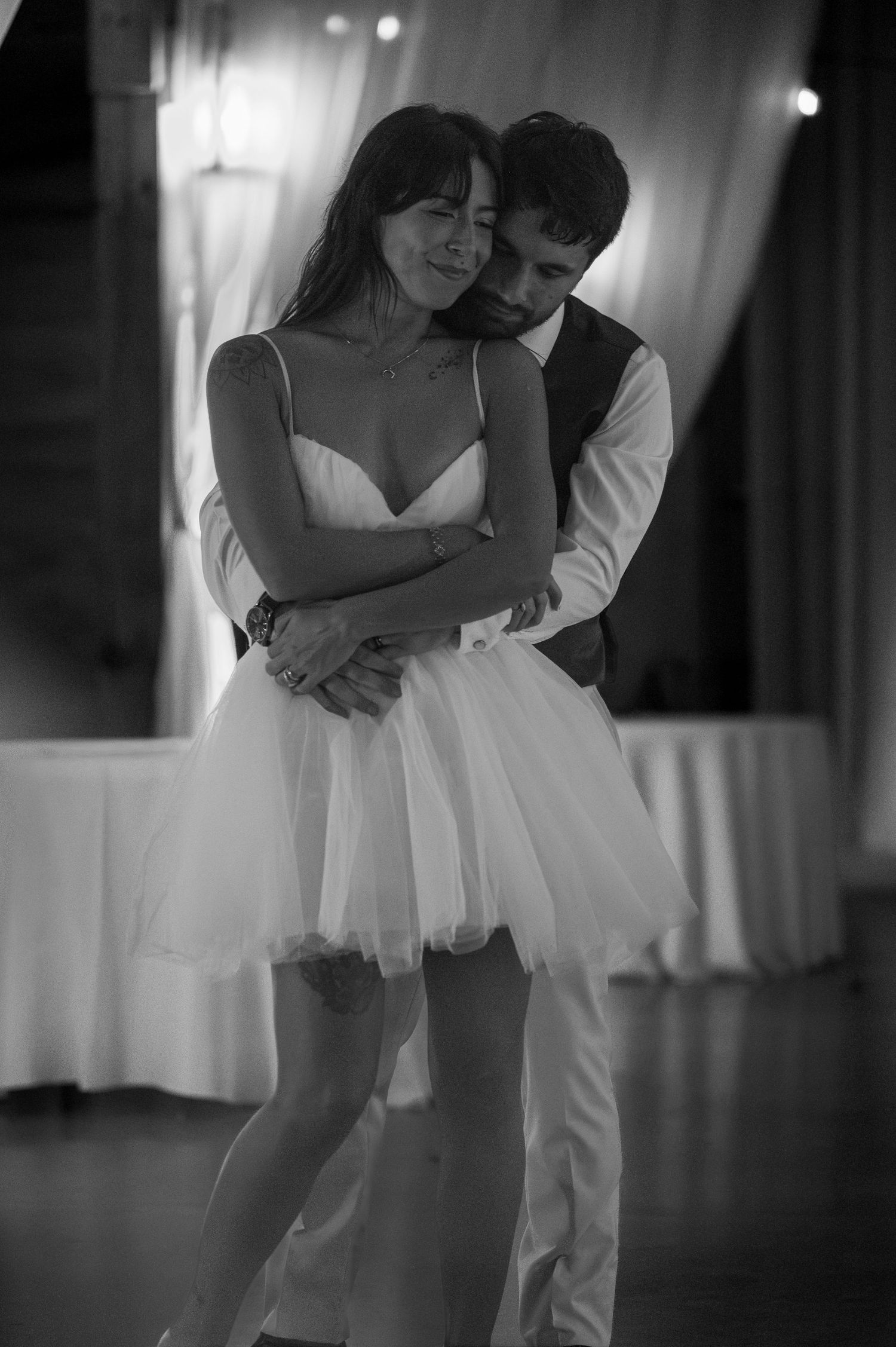 Black and white photo of a couple sharing an intimate first dance, bride in short tulle dress embraced by groom in vest.