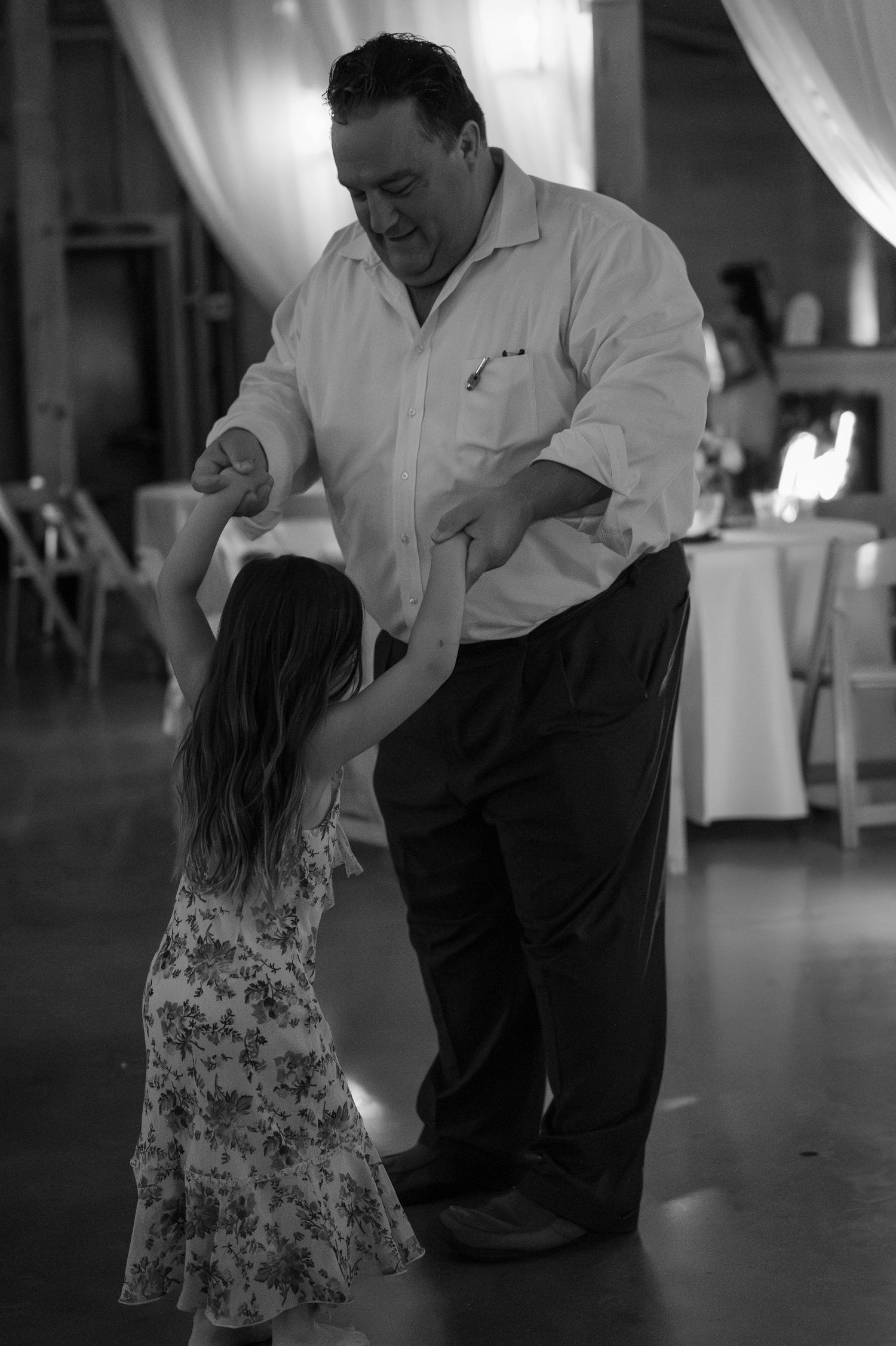 Black and white photo of a man dancing with a young girl at a wedding reception.