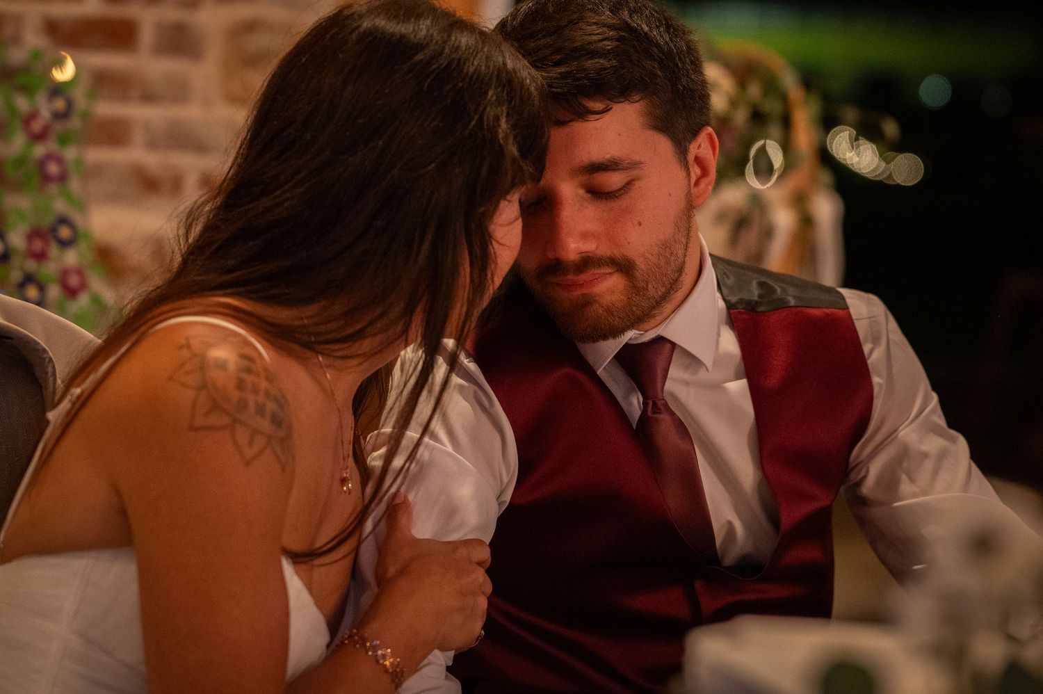 Bride and groom share an intimate emotional moment at their wedding reception, groom wearing a burgundy vest.